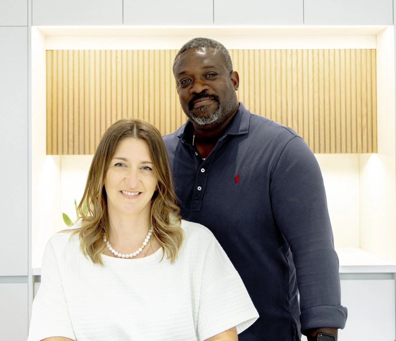 Julie and Chris, the owners of Waterfront Home Improvements, standing together and smiling in a bright, finished room.