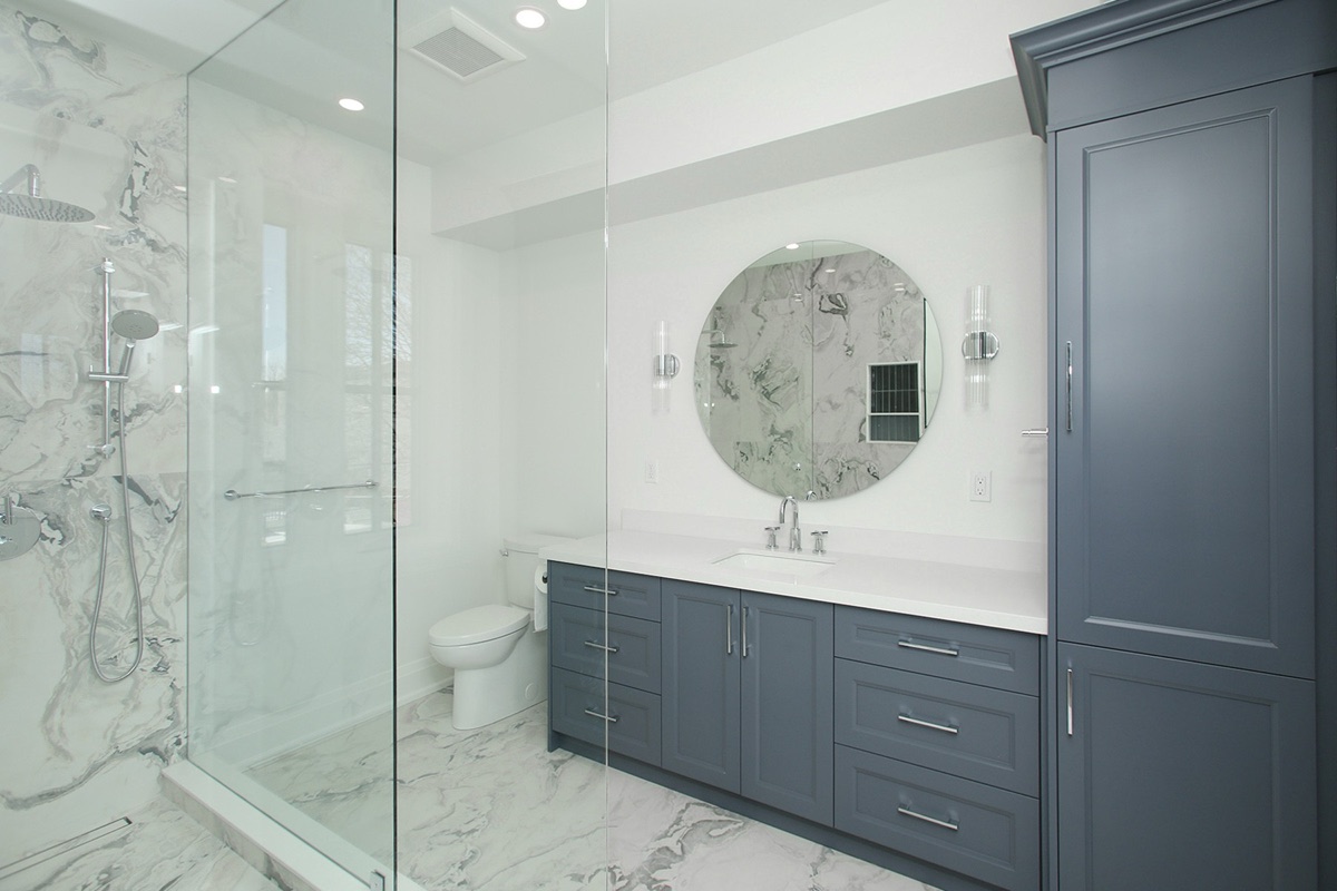 Primary ensuite in Alderwood with book-matched marble walls, walk-in glass shower, and slate blue vanity.