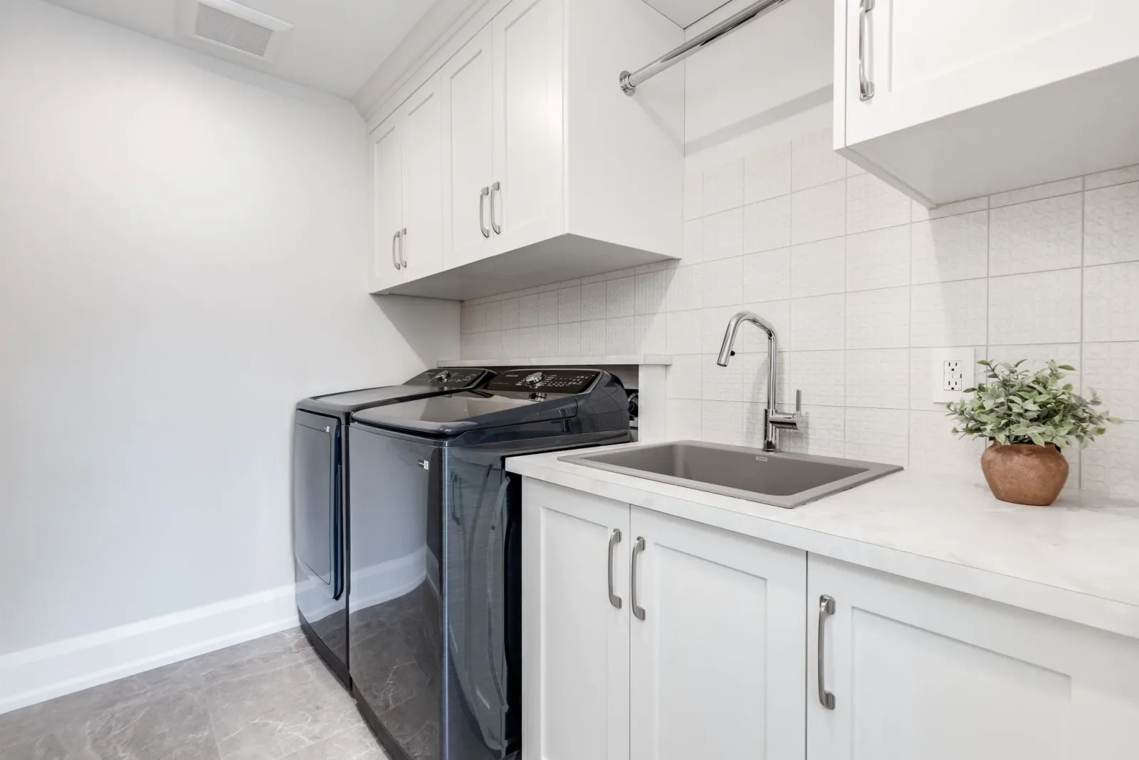 Basement apartment laundry room with stacked washer and dryer, a stainless steel sink, and custom cabinetry, finished by Waterfront Home Improvements in Toronto