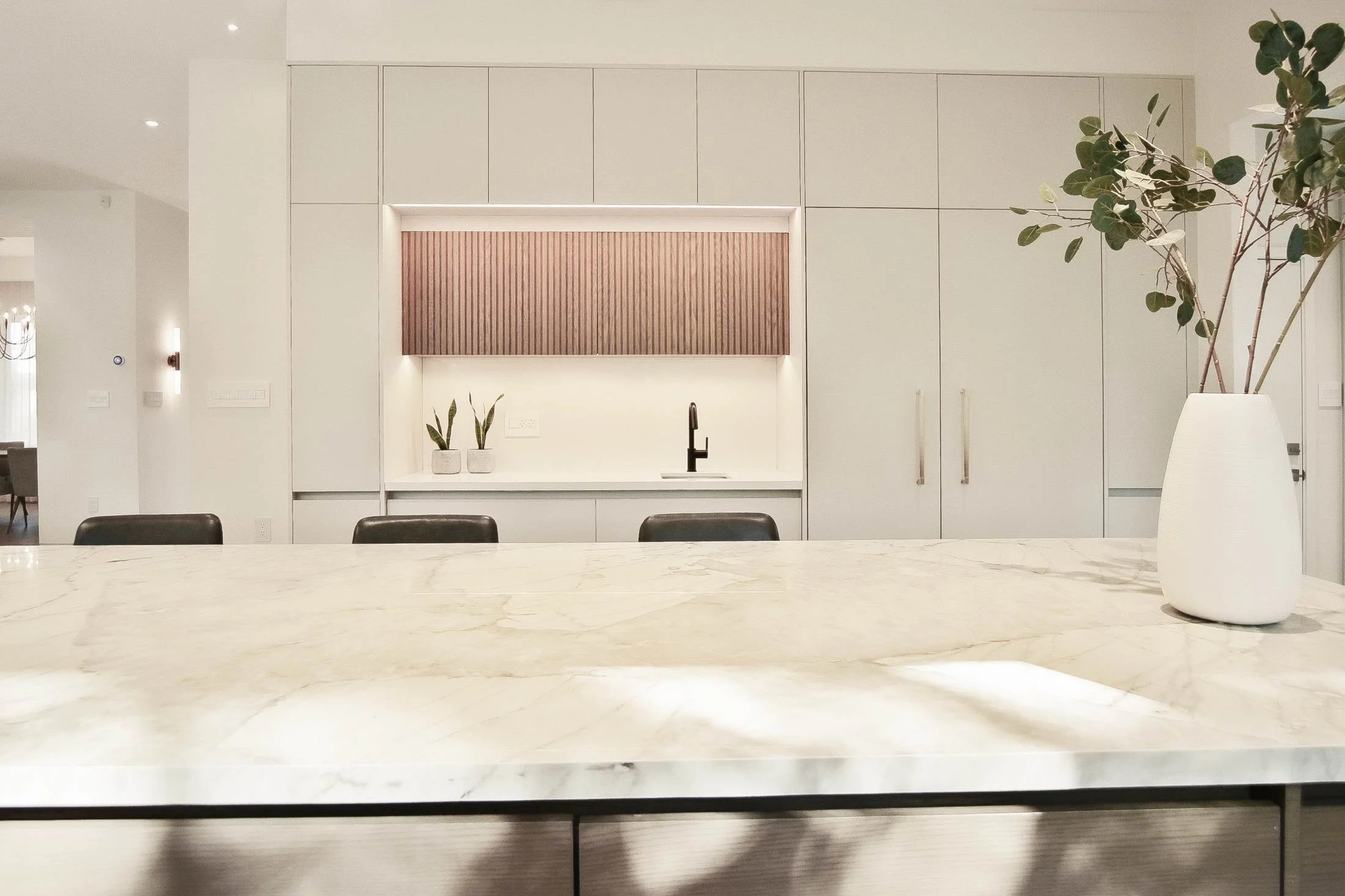 Minimalist kitchen with a marble island, fluted wood niche, and a vase of greenery