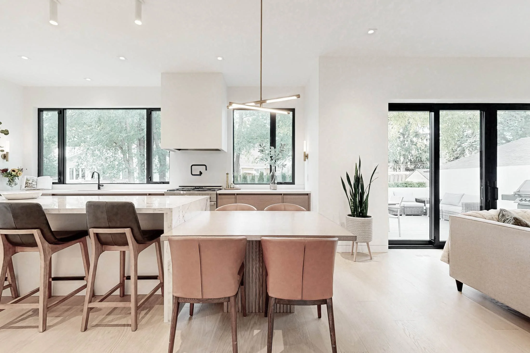 Open living and dining space with an island, blush dining chairs, and floor-to-ceiling black-framed windows