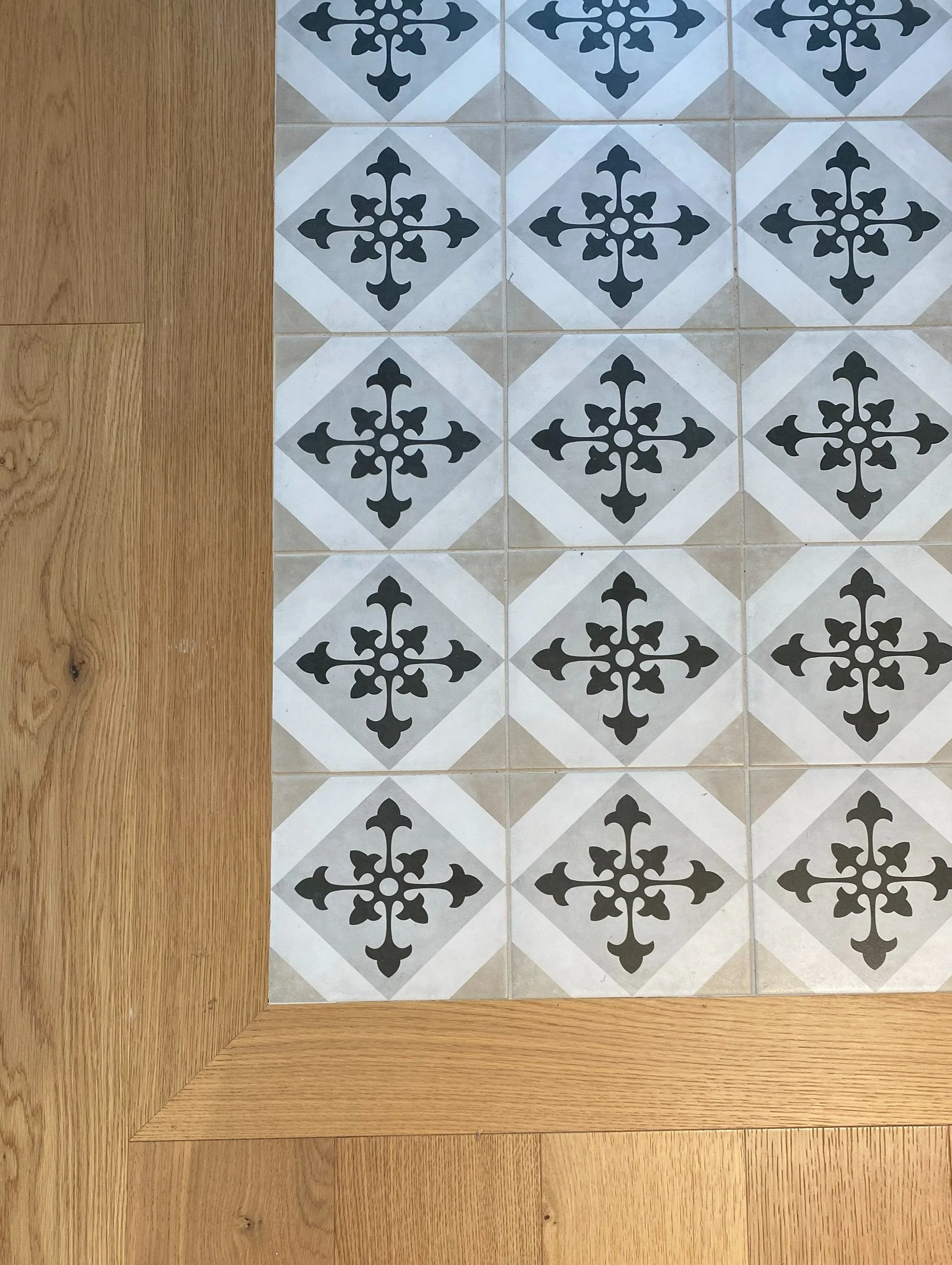 A section of floor with decorative black and white patterned tiles bordered by a wooden floor.