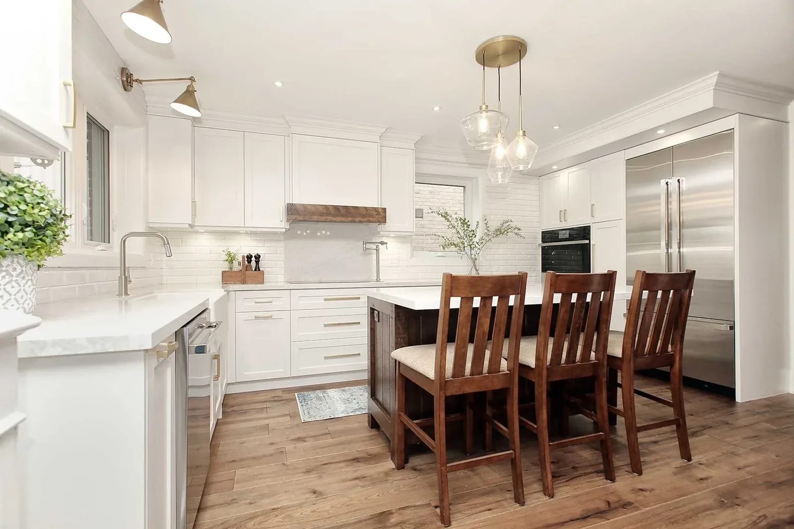 Renovated kitchen with white cabinetry, a wood island with seating, glass pendant lights, and a stainless steel refrigerator.
