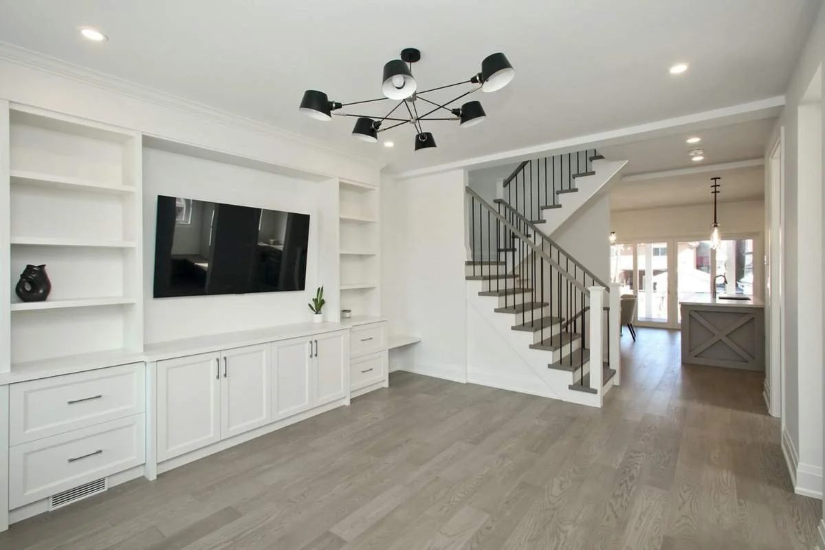 Living room with a white built-in media wall and black chandelier, open to the staircase and kitchen beyond.