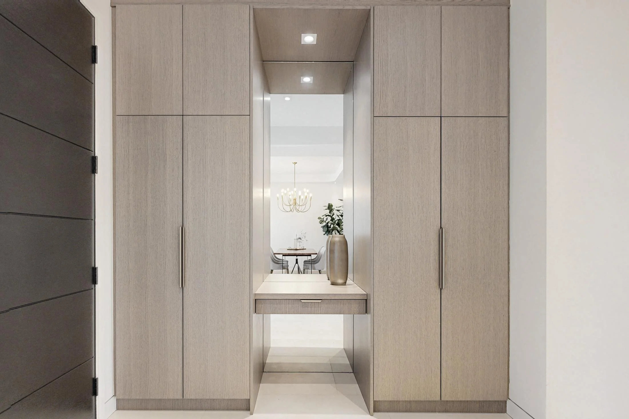 Built-in taupe cabinetry frames a servery niche with a stone counter and fresh flowers.