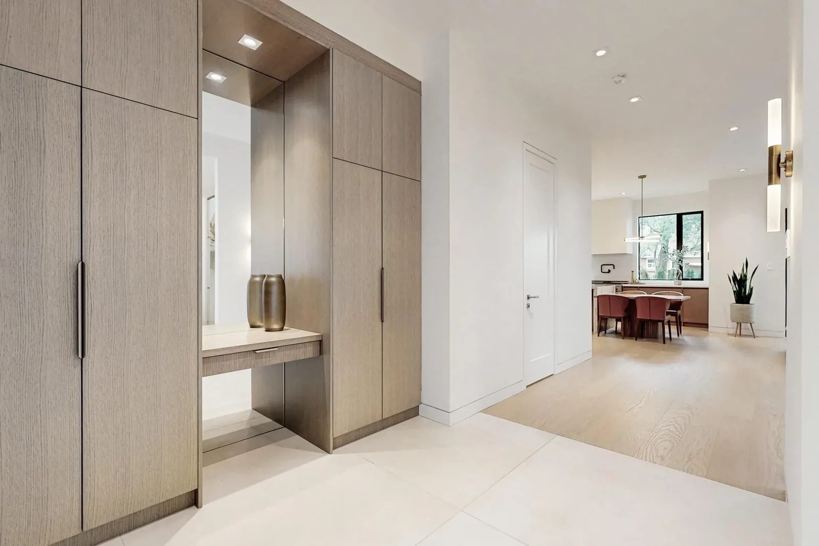 Hallway of built-in taupe cabinetry with a lit niche looking toward the kitchen and dining area.