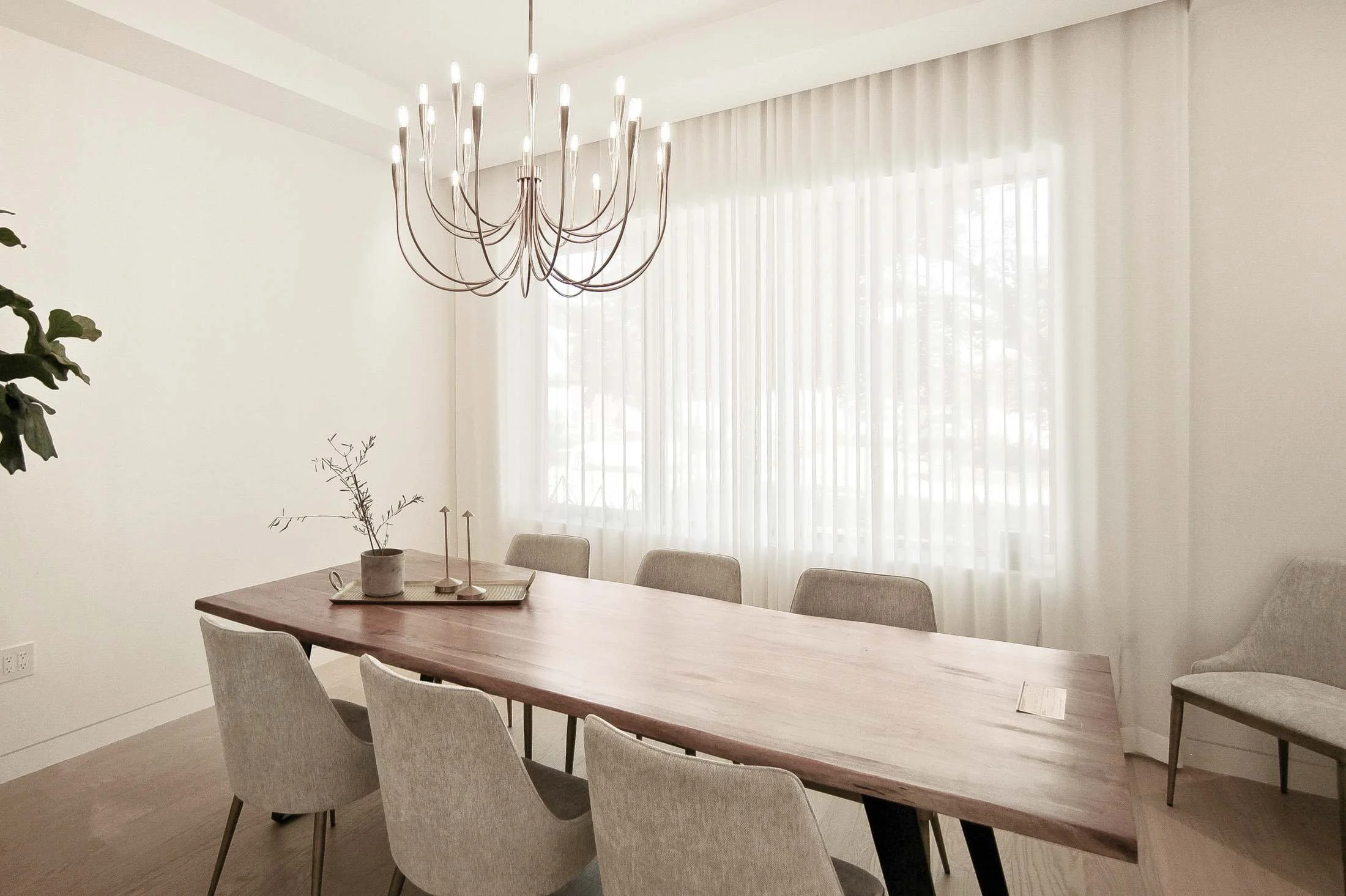 Dining room with a live-edge wood table, upholstered chairs, and a black candelabra chandelier.