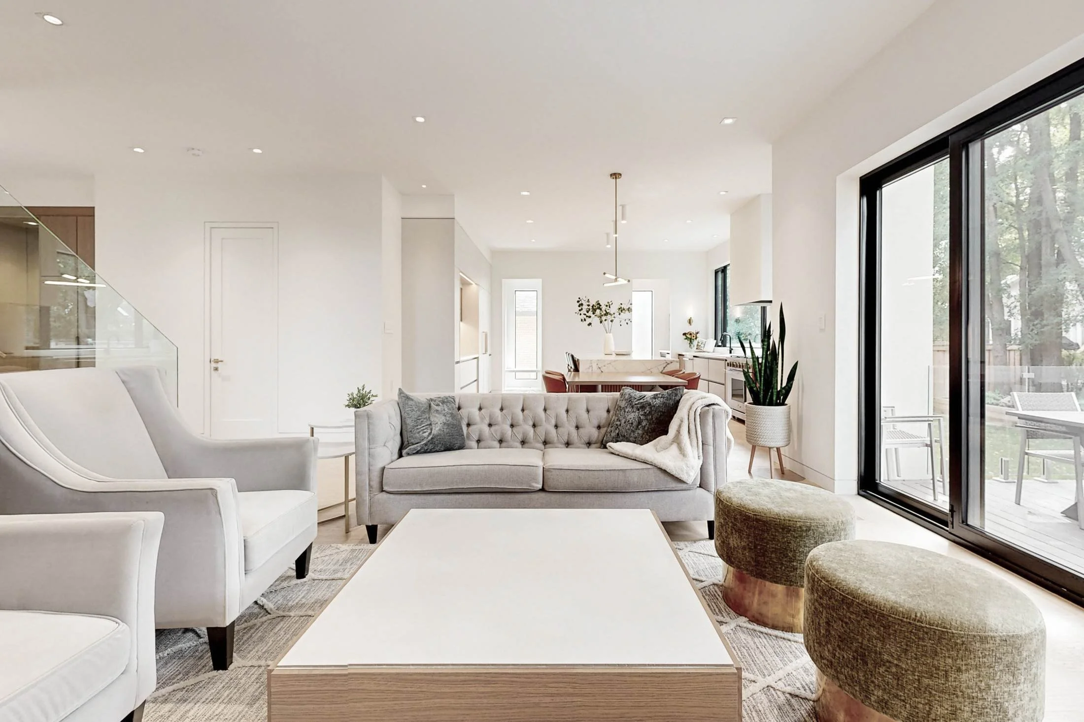 Bright living room with a grey tufted sofa, white armchairs, and green ottomans around a light wood coffee table.