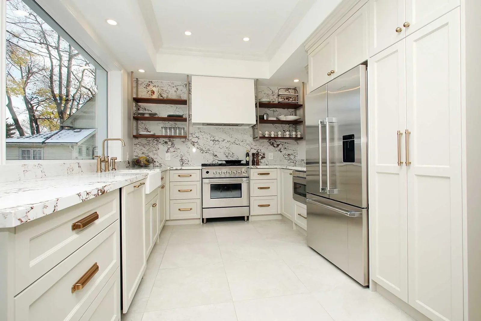 Bright white kitchen with shaker cabinetry, marble surfaces, open wood shelves, and stainless appliances.
