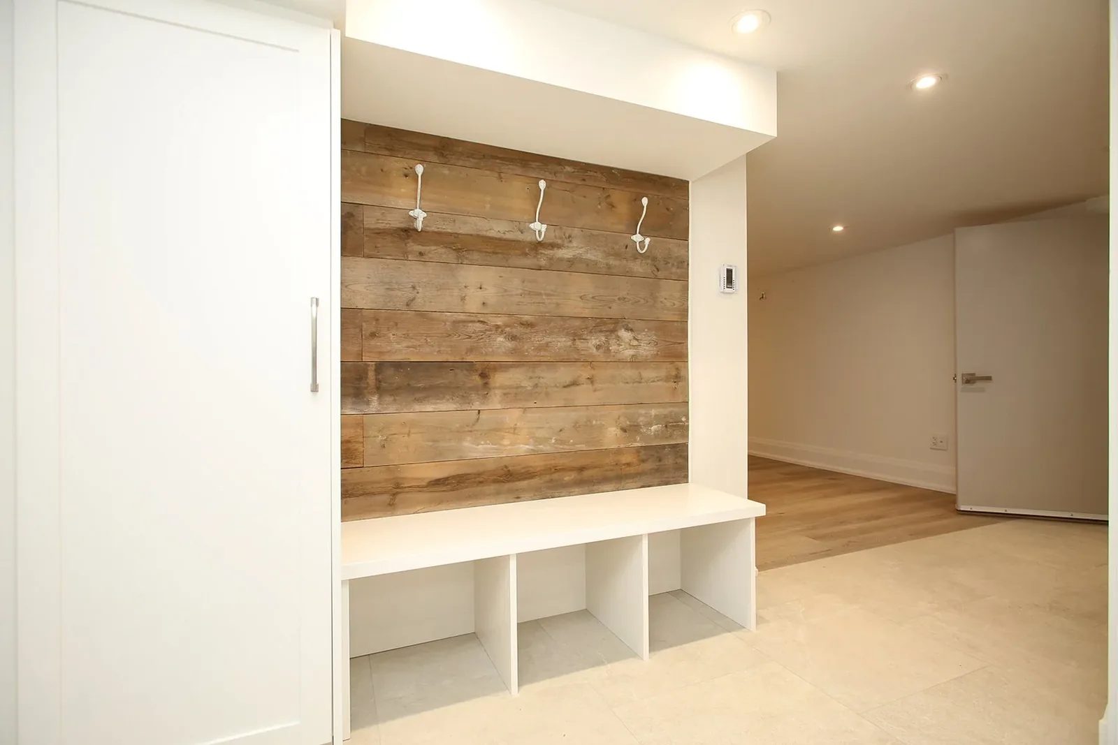Wider finished basement showing the reclaimed plank mudroom nook, built-in bench, and recessed lighting.