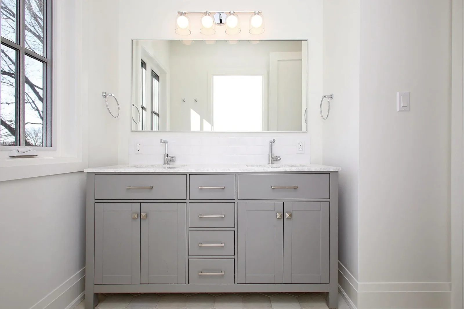 Main bath double-sink grey vanity with Carrara marble top, framed mirror, and four-bulb chrome fixture.