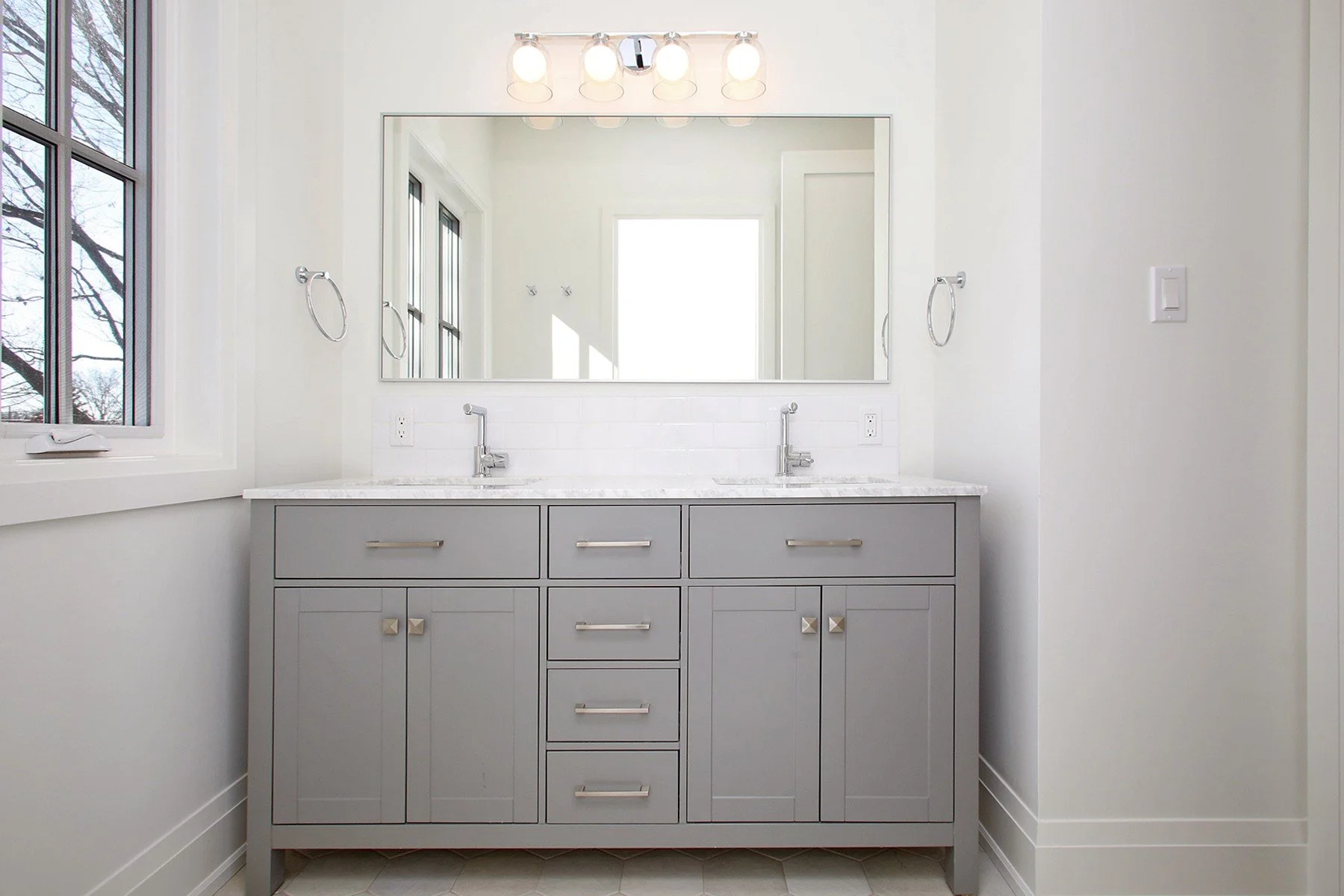 Main bath double-sink grey vanity with Carrara marble top, framed mirror, and four-bulb chrome fixture.