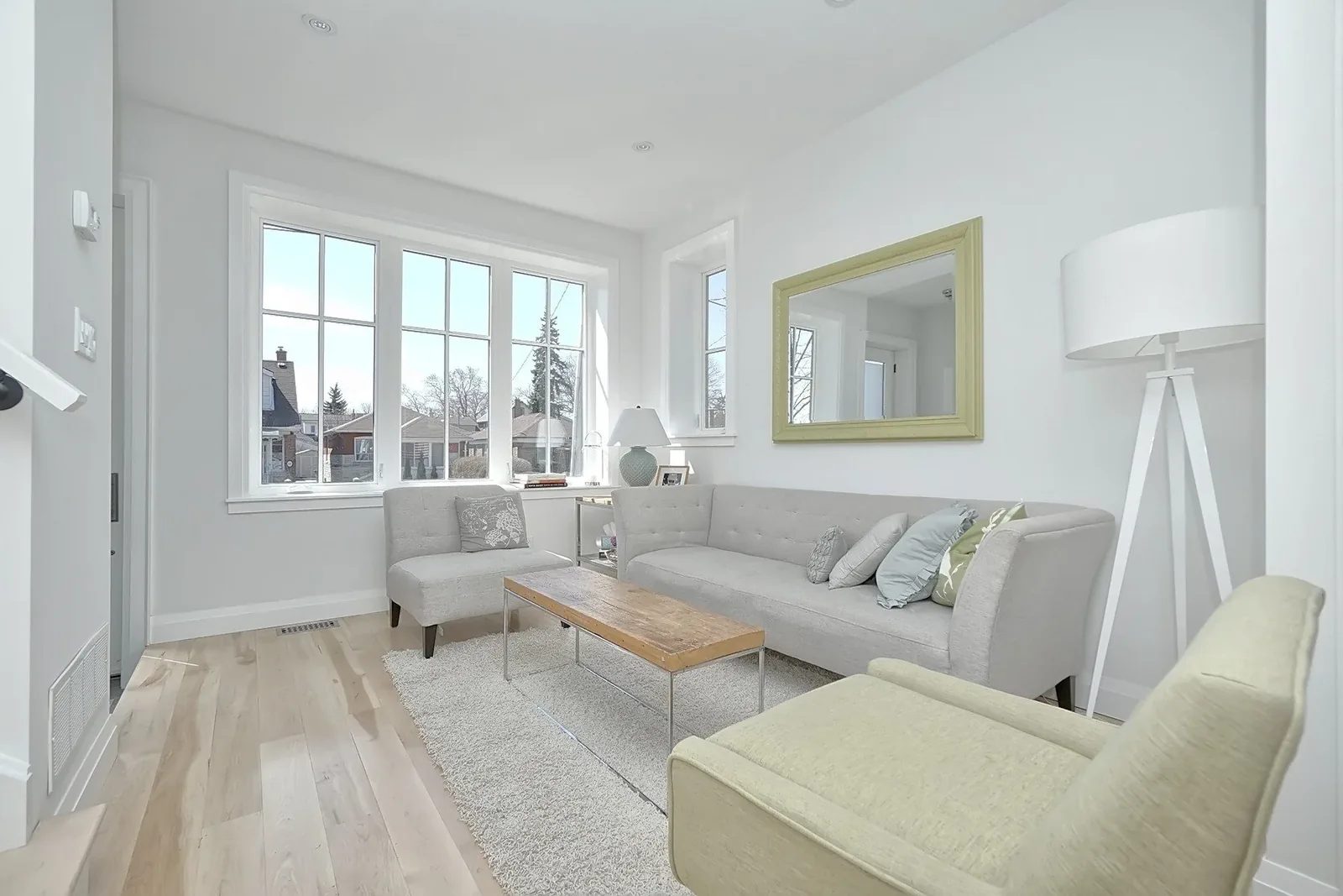 Bright Toronto living room with pale hardwood floors, large front windows, grey seating and warm wood accents.