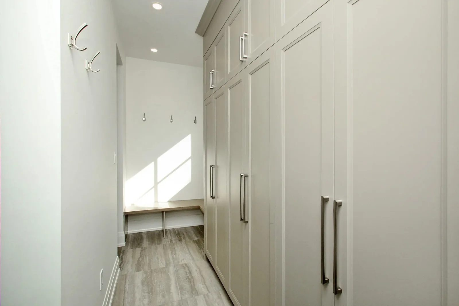 Mudroom with warm grey floor to ceiling cabinets, chrome bar pulls, coat hooks, and a built in bench.