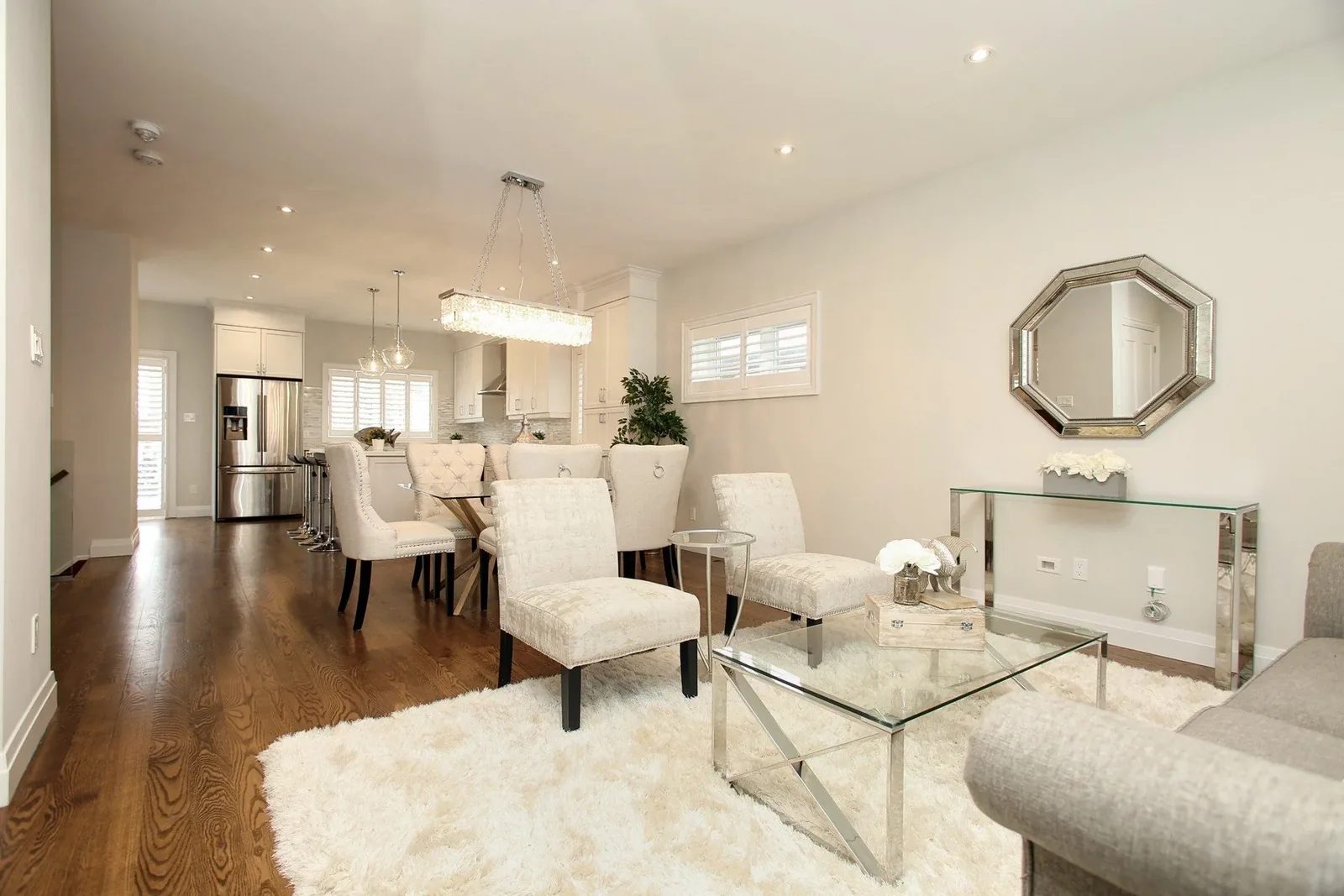 Open concept living, dining, and kitchen space with dark wood floors, white seating, and glass doors.