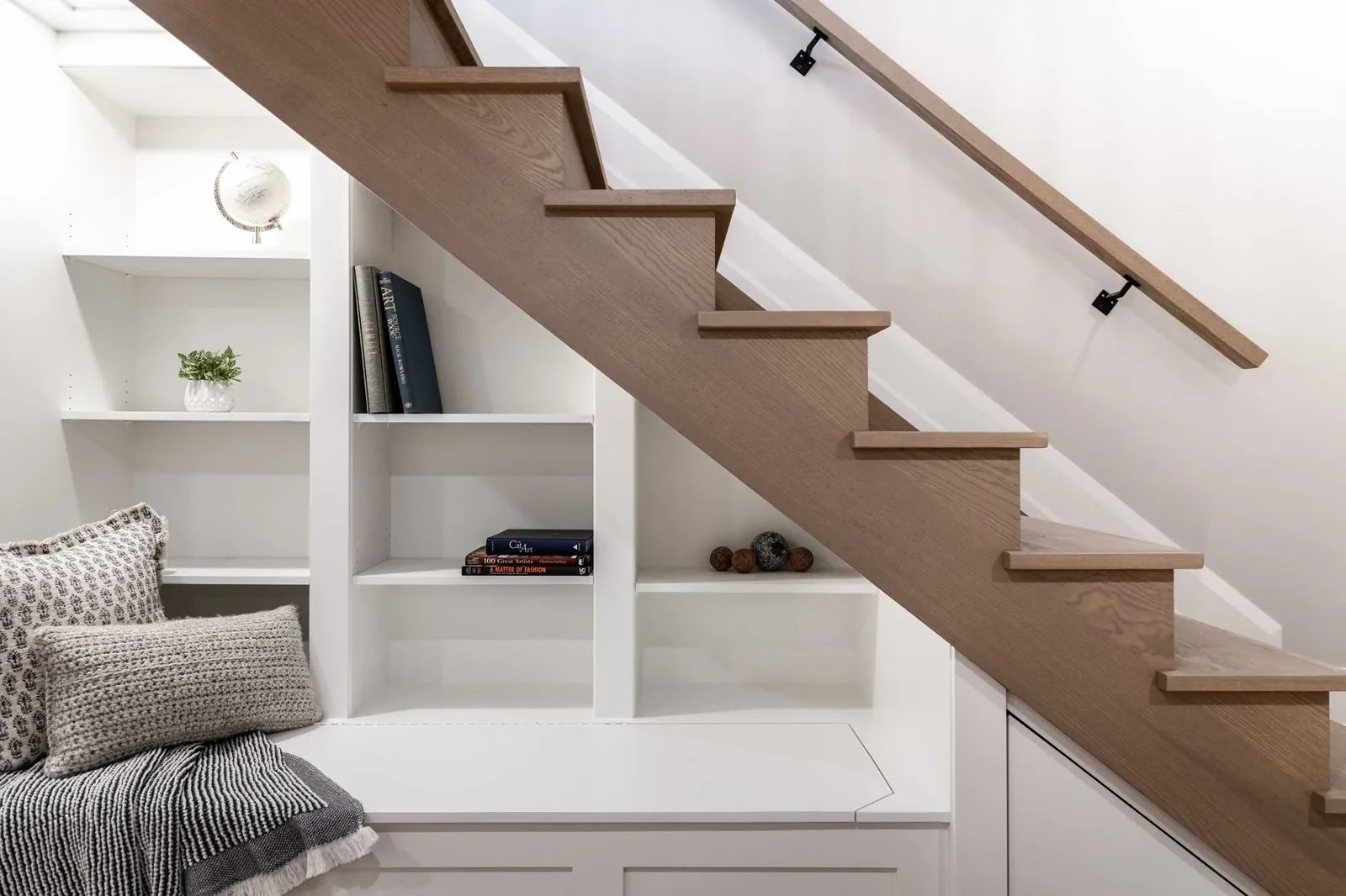 Custom under-stair shelving and natural oak stairs create an organised warm white hallway nook.