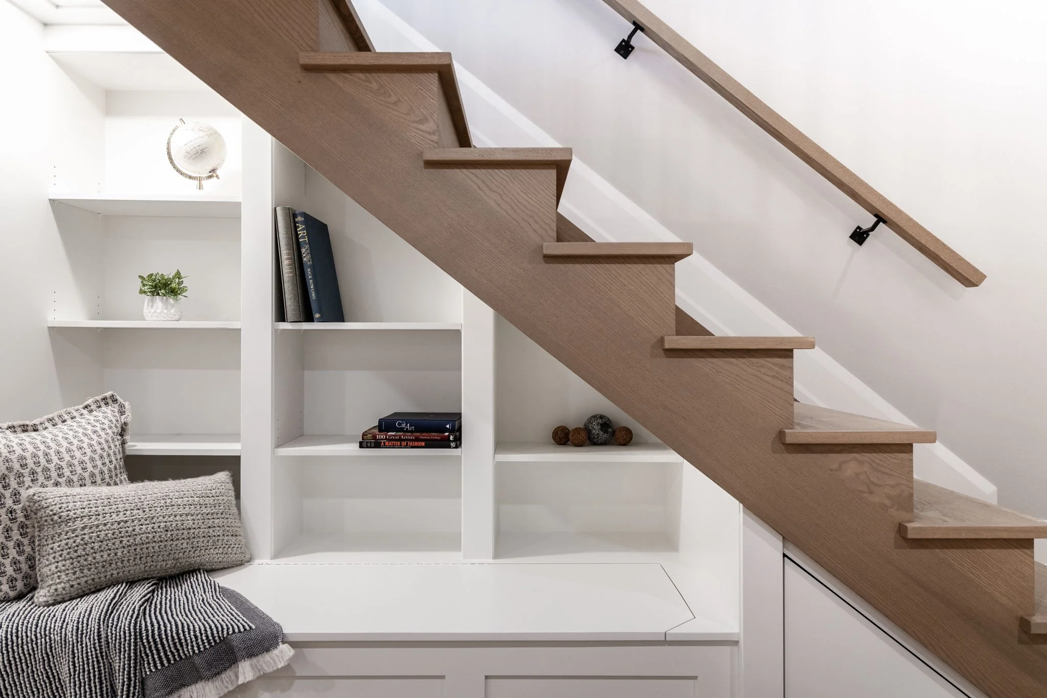Custom under-stair shelving and natural oak stairs create an organised warm white hallway nook.