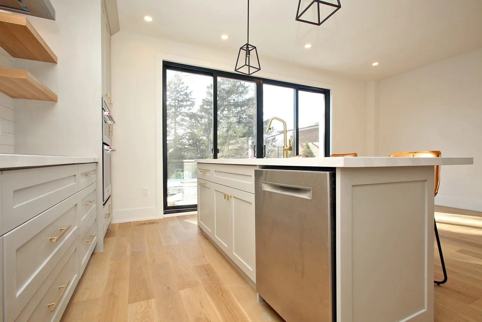 Bright warm white kitchen with oak flooring, brass accents, black framed doors, and a large island.