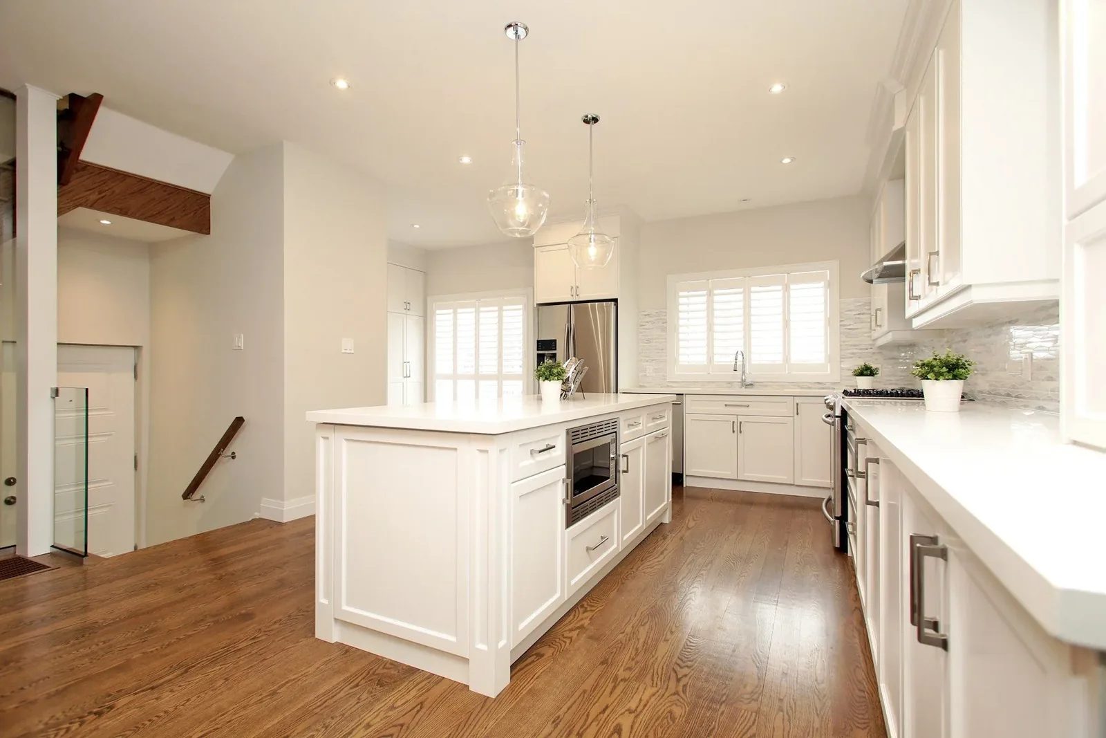 Bright white kitchen with a large centre island, warm wood floors and glass pendants.