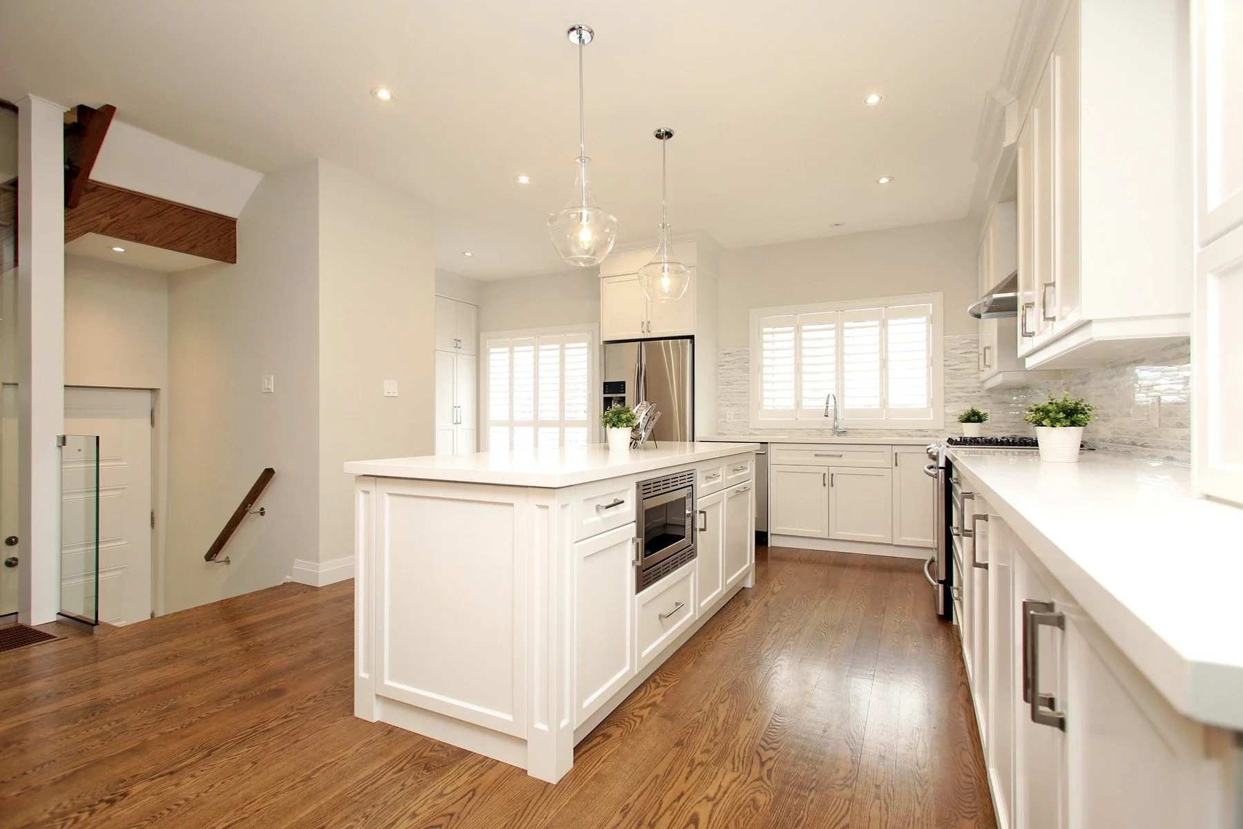Bright white kitchen with a large centre island, warm wood floors and glass pendants.