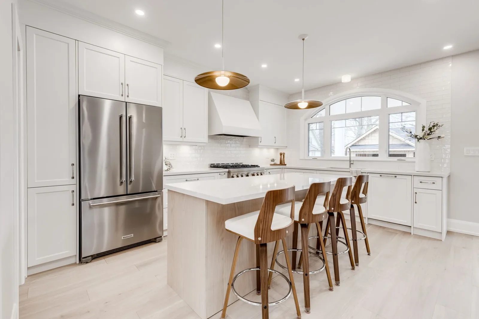 Bright Toronto kitchen renovation with white shaker cabinetry, quartz island, oak seating and a window over the sink.