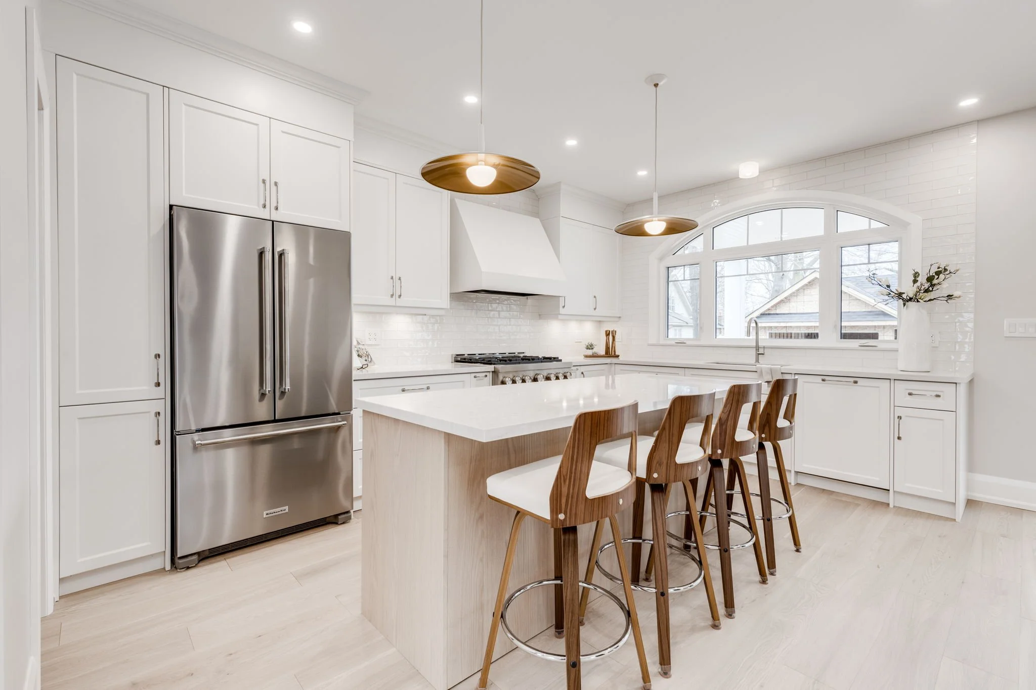 Bright Toronto kitchen renovation with white shaker cabinetry, quartz island, oak seating and a window over the sink.