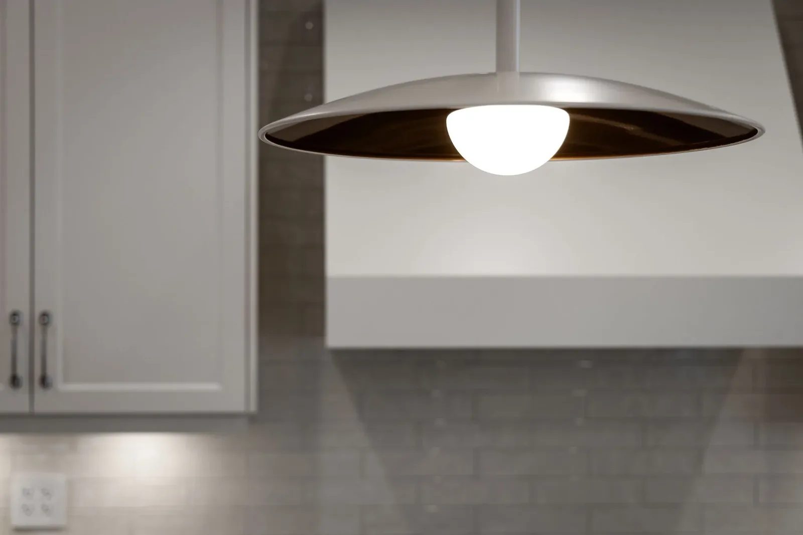 Warm white pendant light above a grey tile backsplash and white kitchen cabinetry.