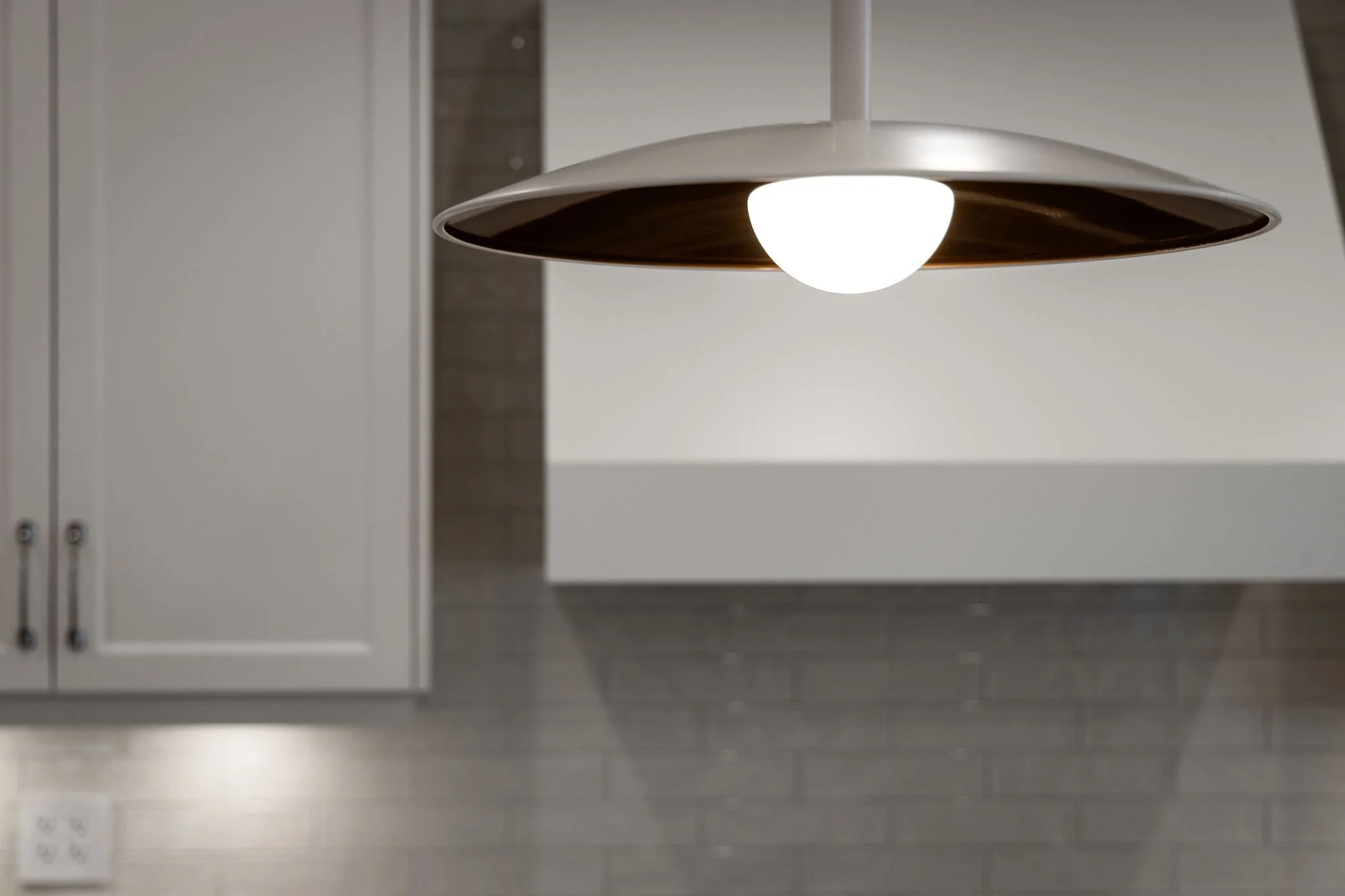 Warm white pendant light above a grey tile backsplash and white kitchen cabinetry.