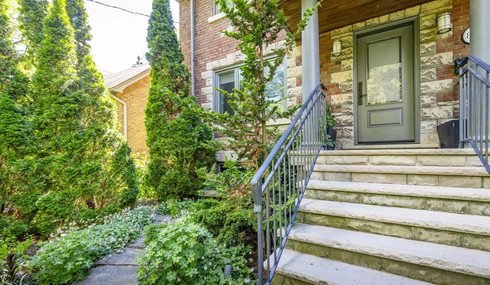 Stone front steps with a black iron railing leading to the covered porch of a brick-and-stone Swansea home near High Park.