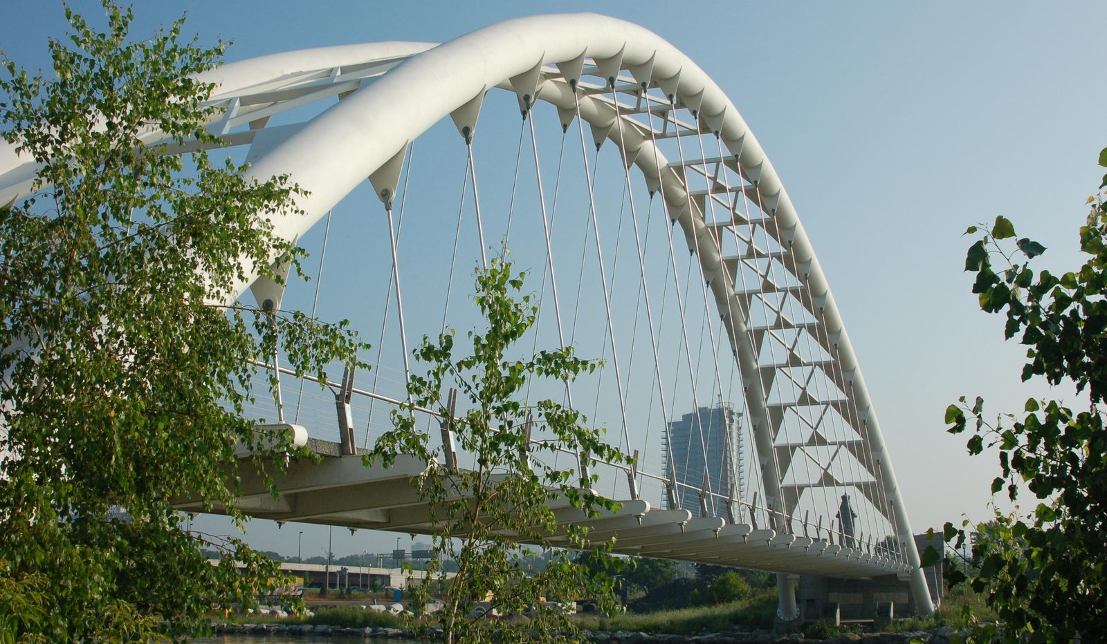 The white Humber Bay Arch Bridge spanning the water, framed by trees under a blue sky.