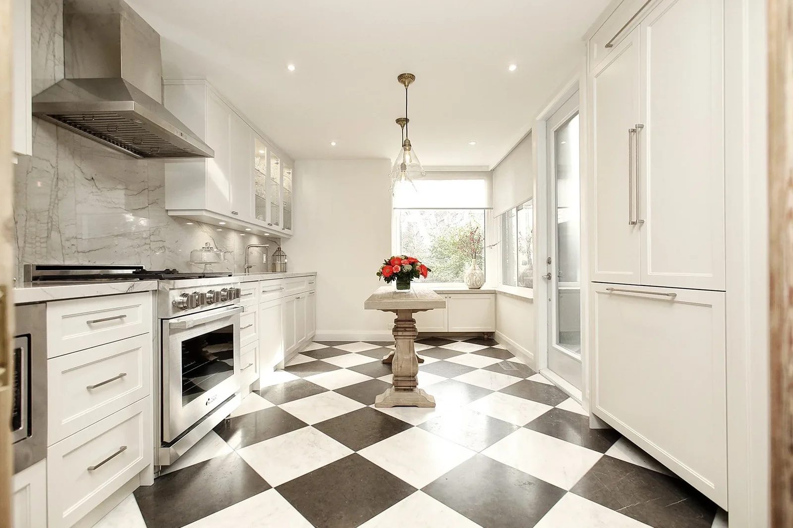 Bright white galley kitchen with checkerboard tile, stone surfaces, and a small centre table.