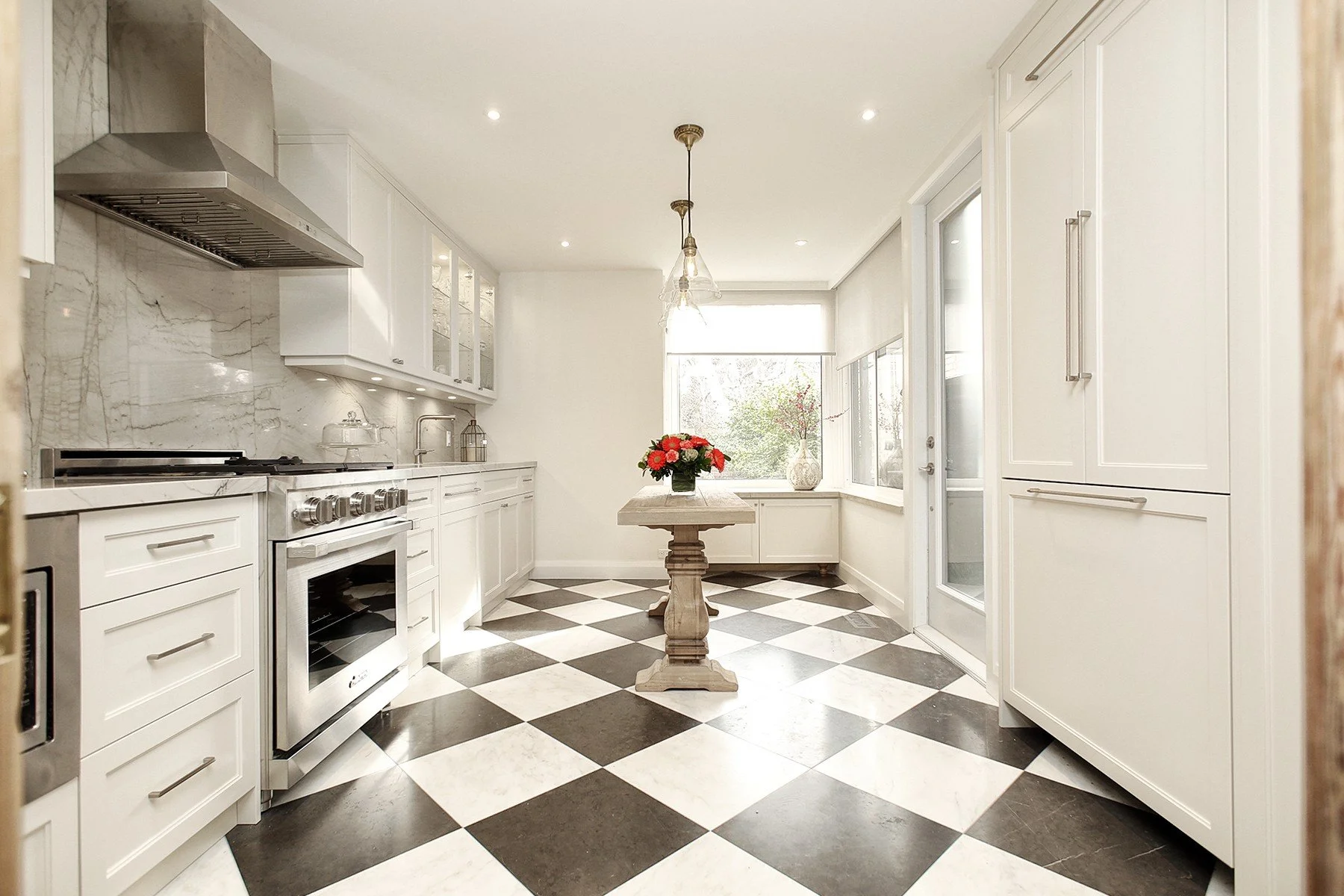 Bright white galley kitchen with checkerboard tile, stone surfaces, and a small centre table.
