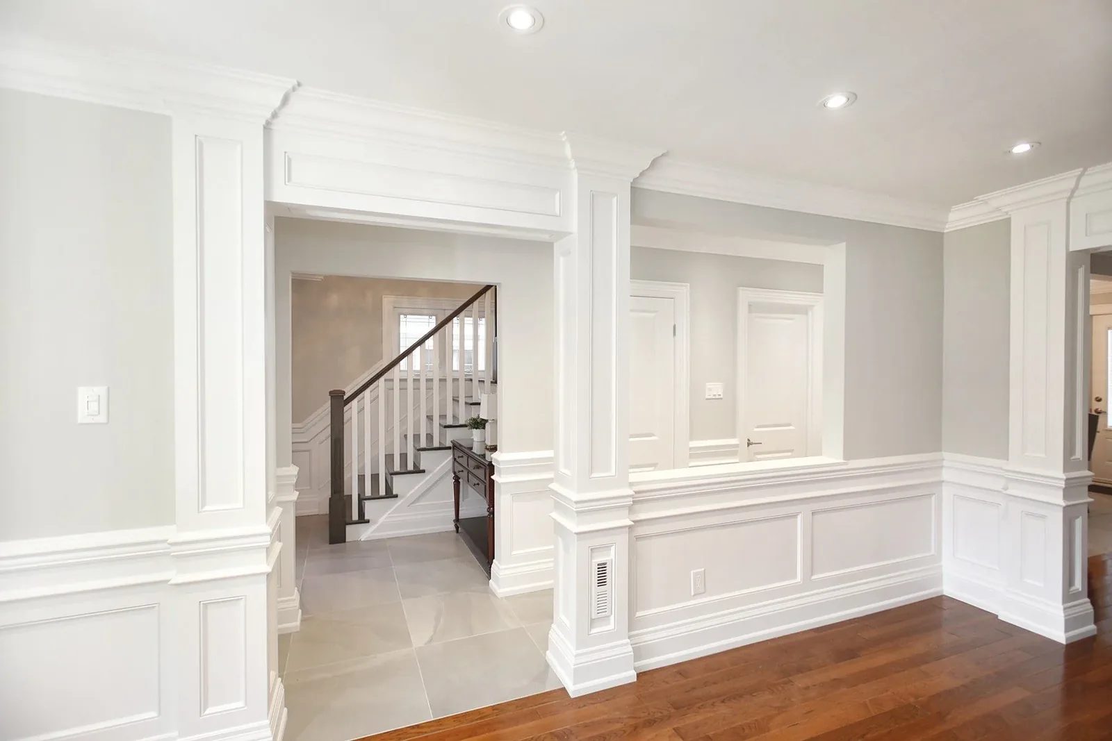 Bright entry hall with panelled millwork, grey walls, hardwood floors, and staircase beyond.