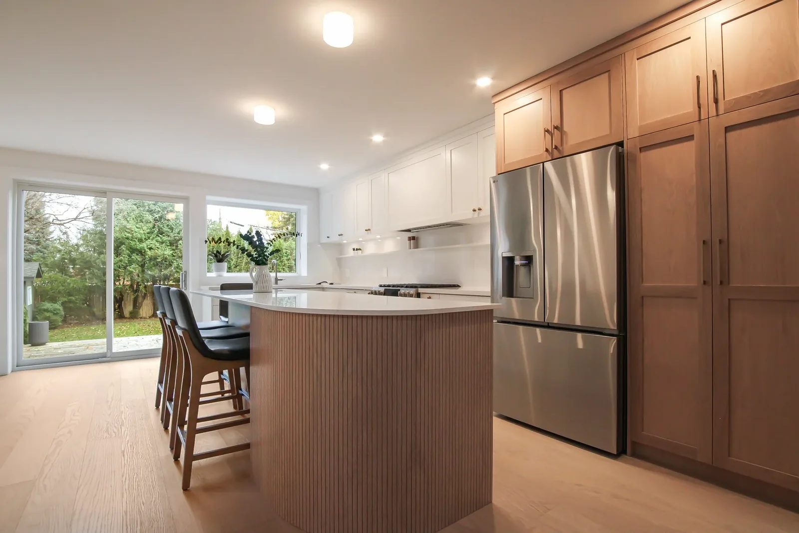 Bright renovated kitchen with white cabinetry, a wood wrapped island, stainless fridge and garden window.