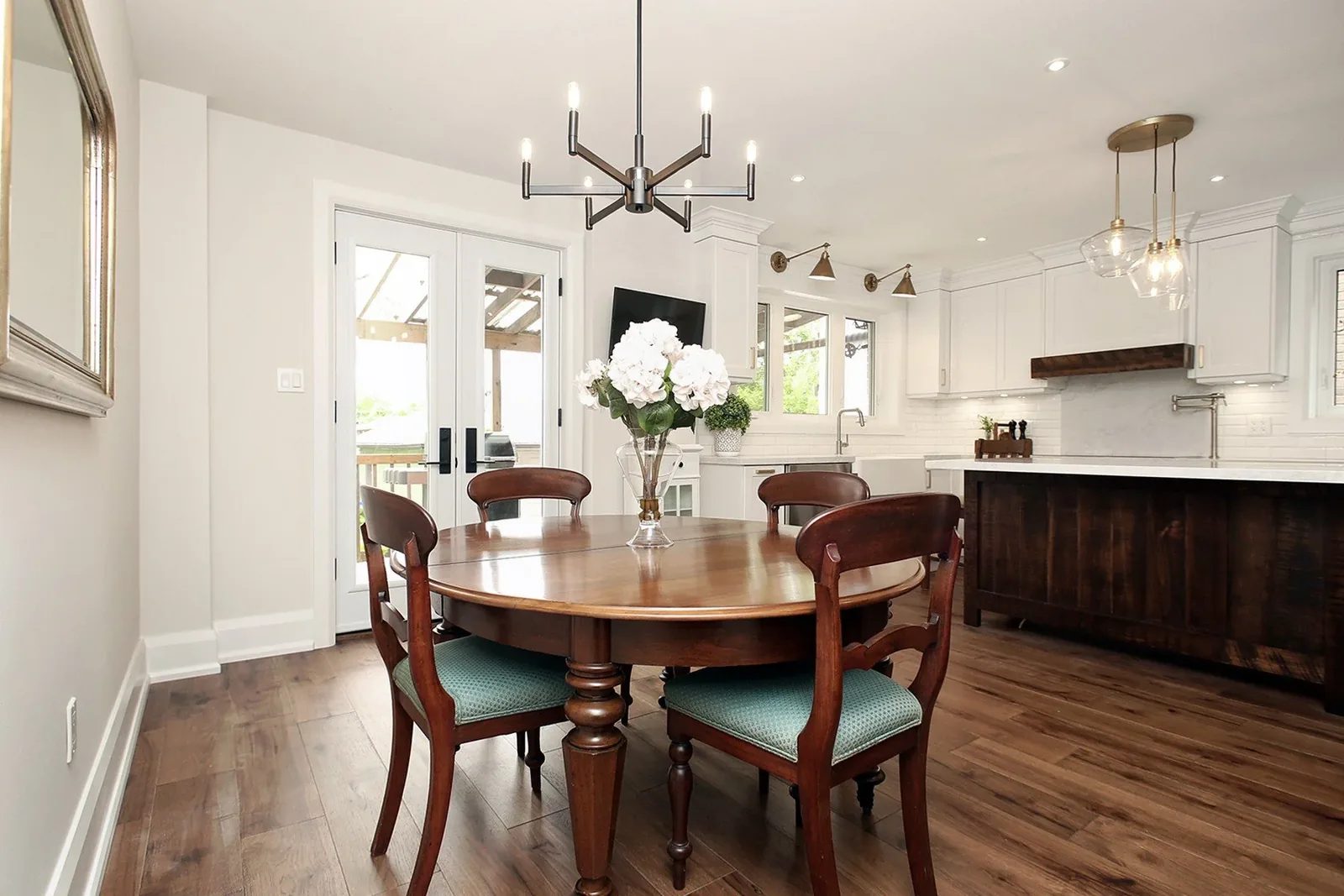 Renovated open concept kitchen and dining room with white cabinets, a dark wood island, and a table by the window.