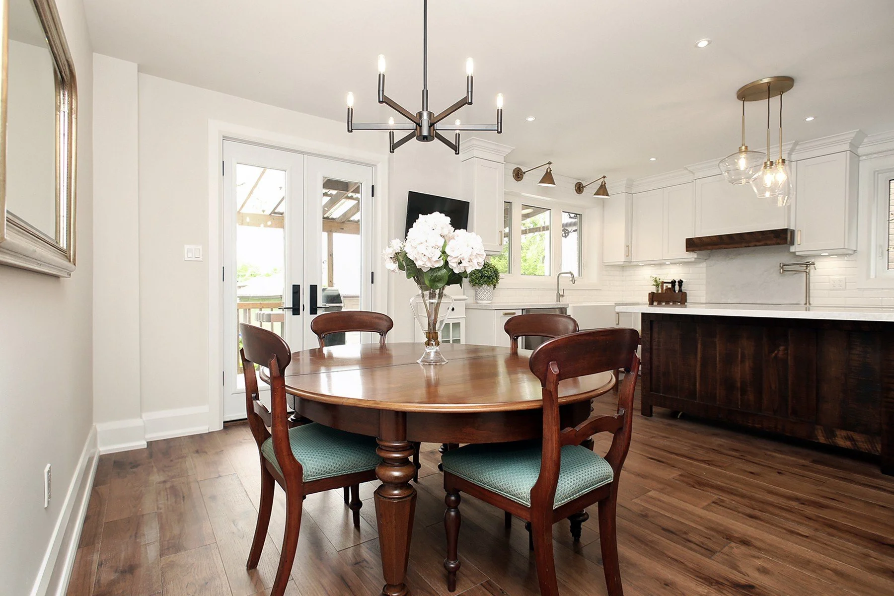 Renovated open concept kitchen and dining room with white cabinets, a dark wood island, and a table by the window.