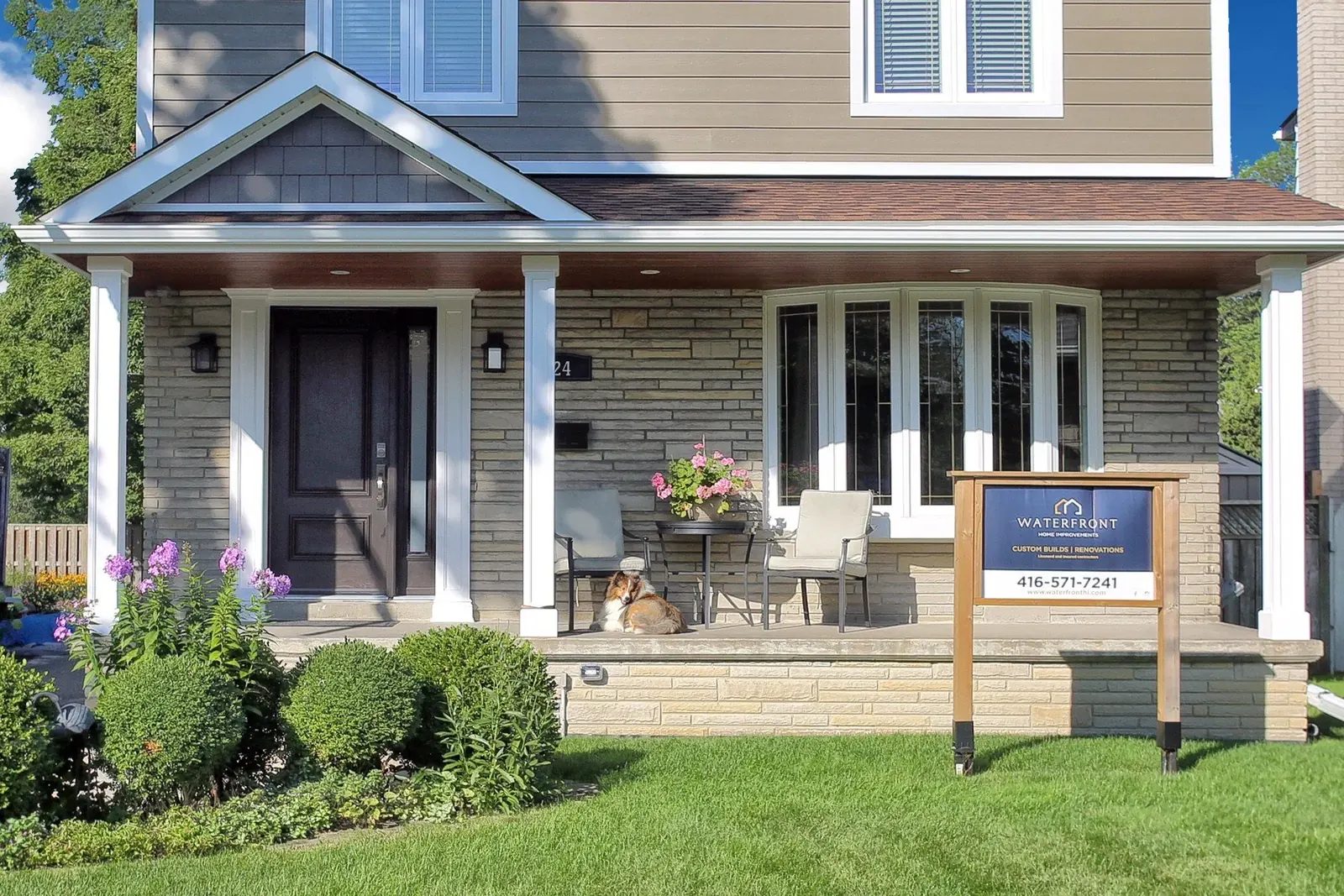 Finished front exterior with stone veneer, a covered porch, bay window and branded sign on a suburban street.