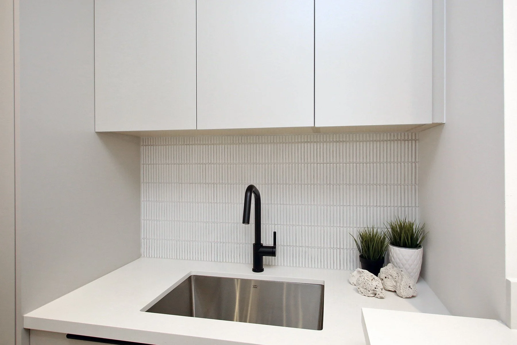 Matte white laundry wet counter with a black faucet over a stainless sink against a vertical kit-kat tile backsplash.