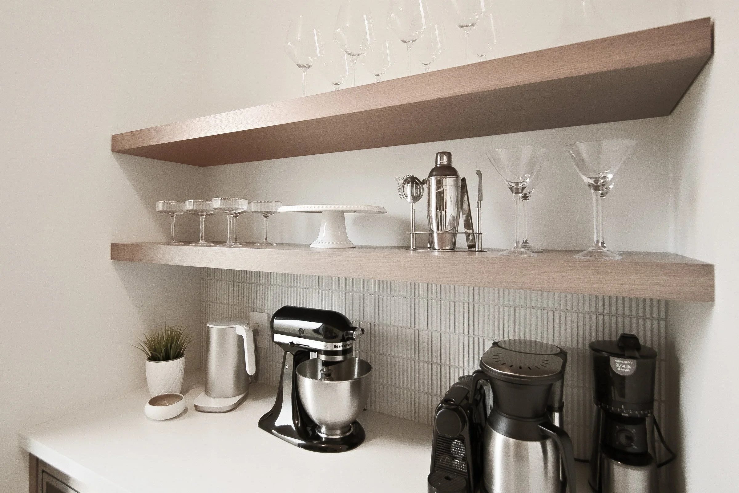 Butler pantry detail with floating oak shelves styled glassware and stacked white tile backsplash.