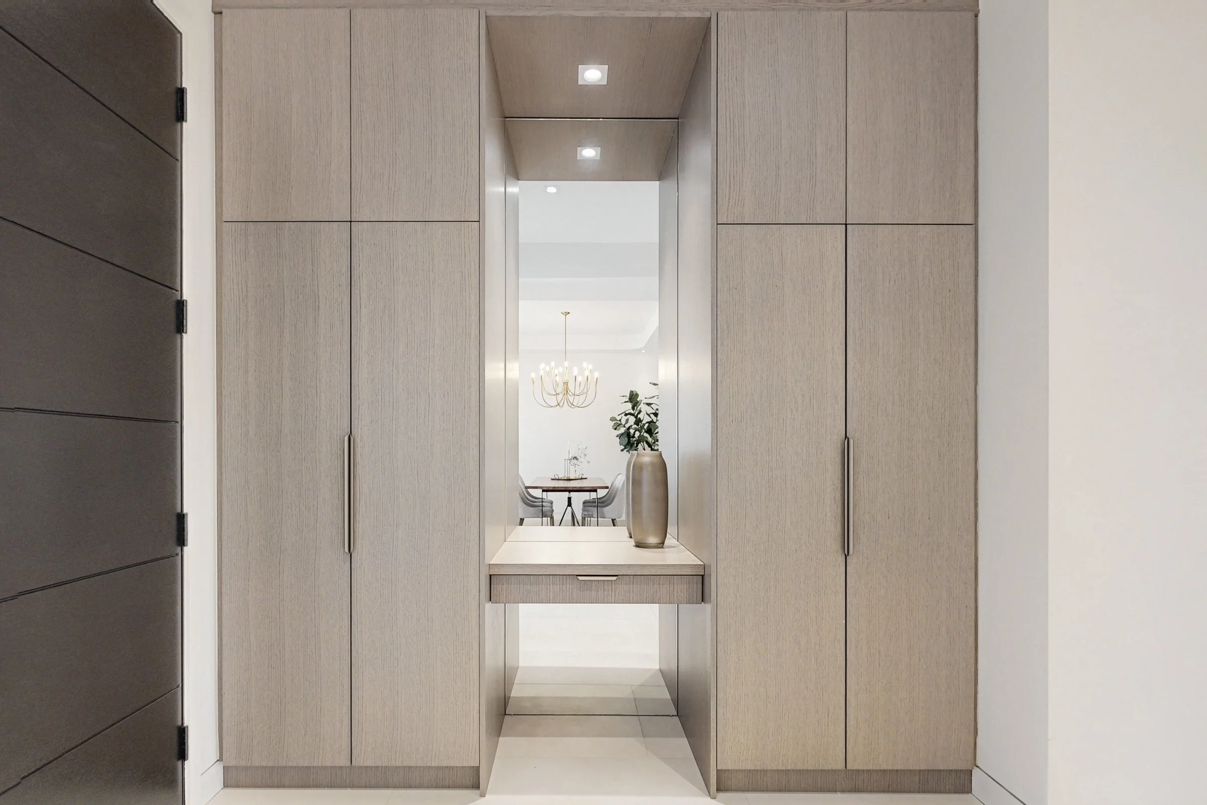 Symmetrical oak wardrobe wall with a mirrored centre niche reflecting the dining chandelier.