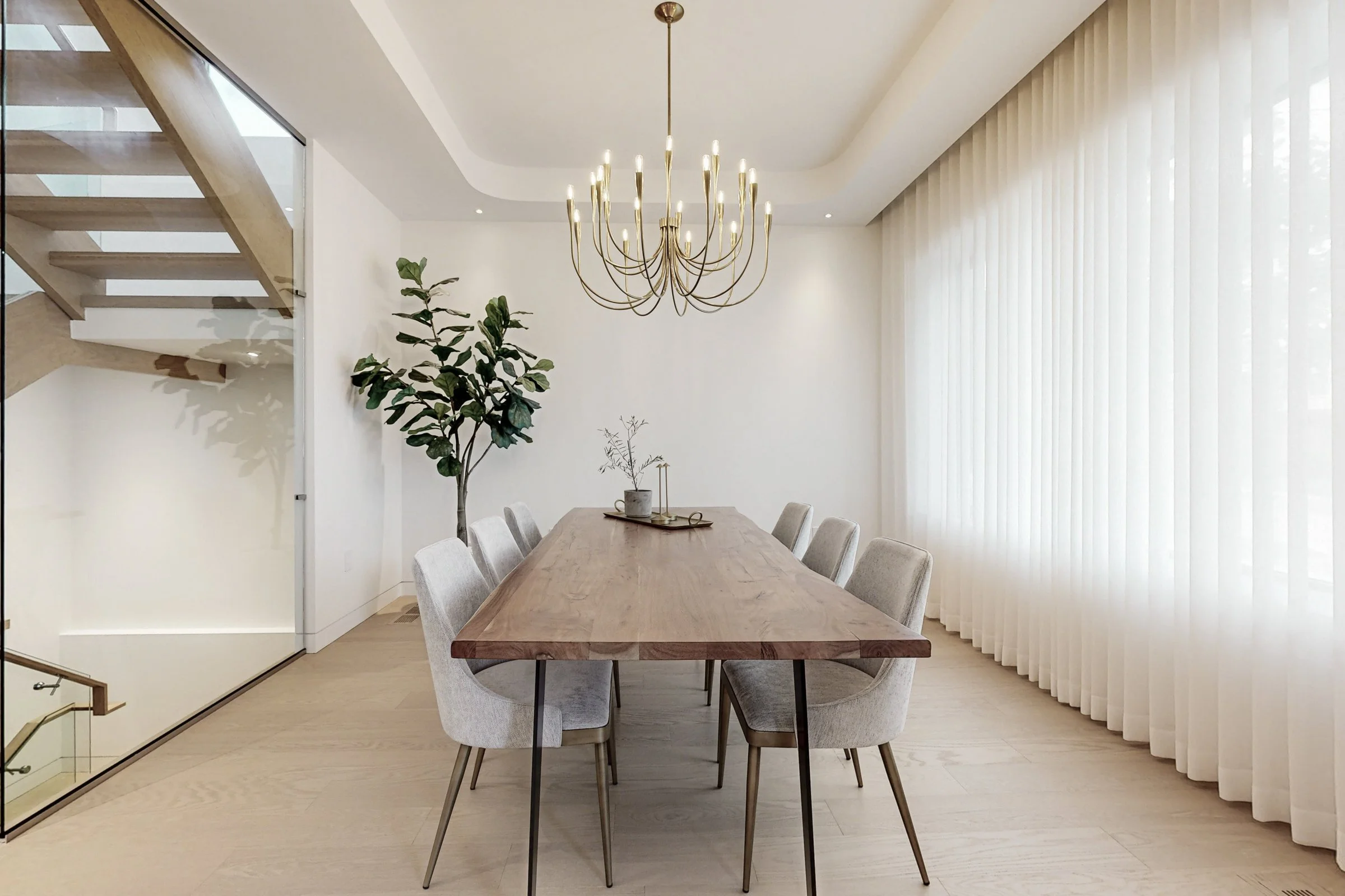 Dining room viewed from the stair side with a wall of linen sheers softening the brass candelabra chandelier.