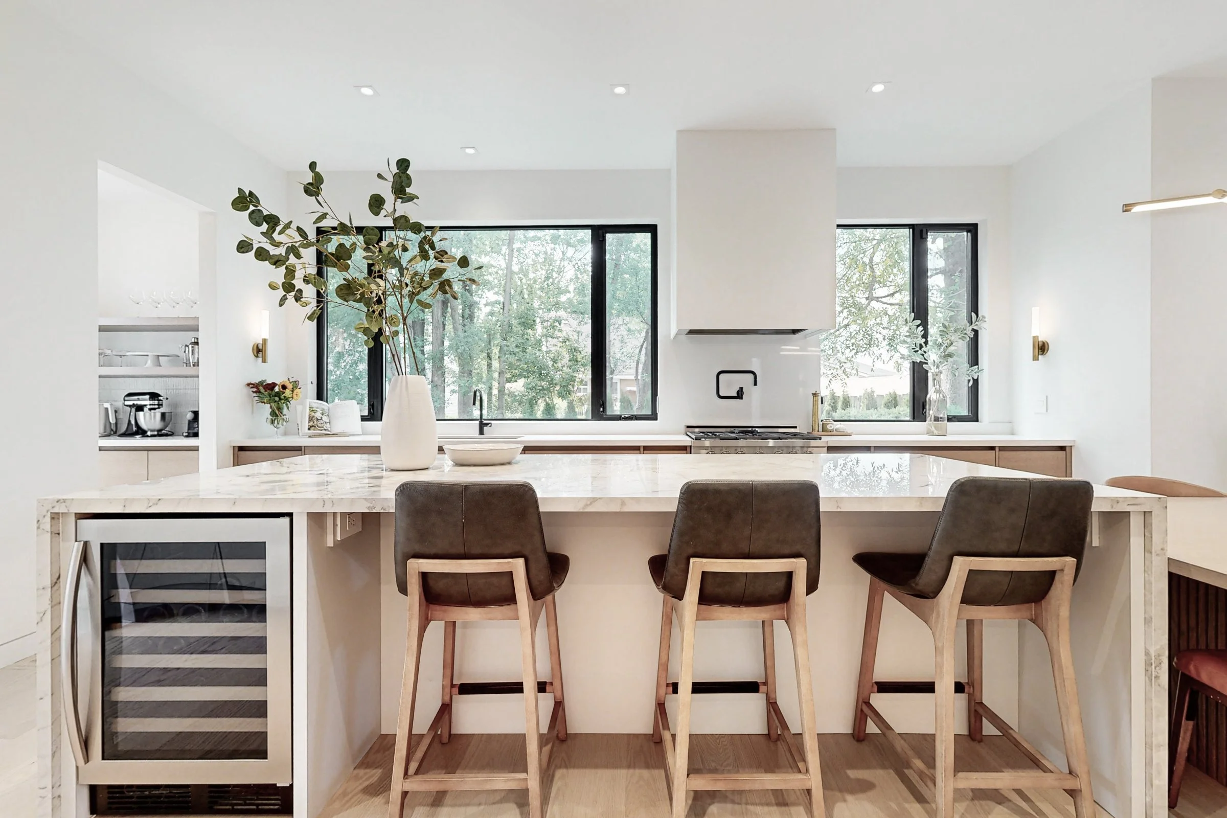 Luxury kitchen island in calacatta marble with waterfall edge leather barstools and black framed windows over the range.