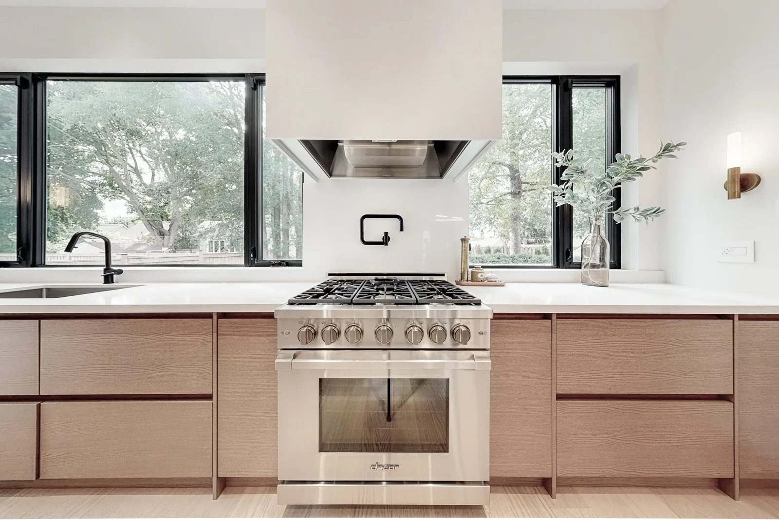 Professional stainless gas range framed by light oak cabinetry and black framed picture windows.