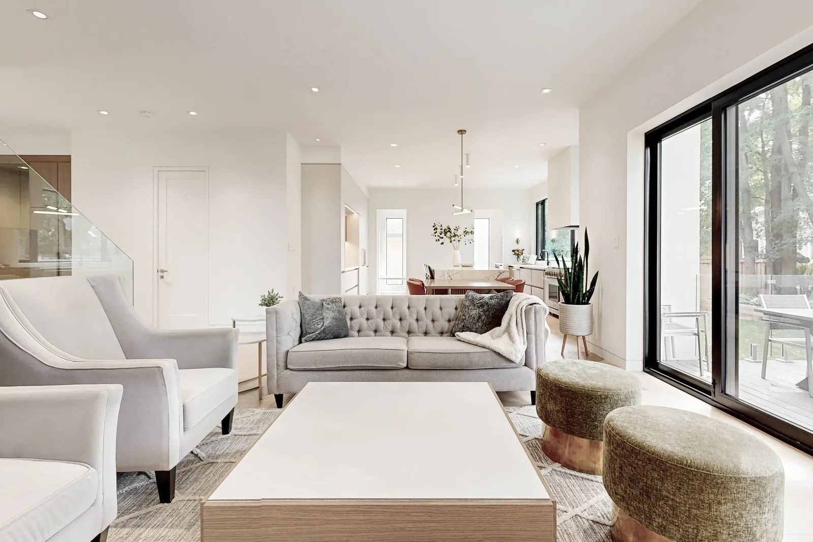 Open concept living room with tufted sofa facing the kitchen and a wall of black-framed sliding doors to the deck.