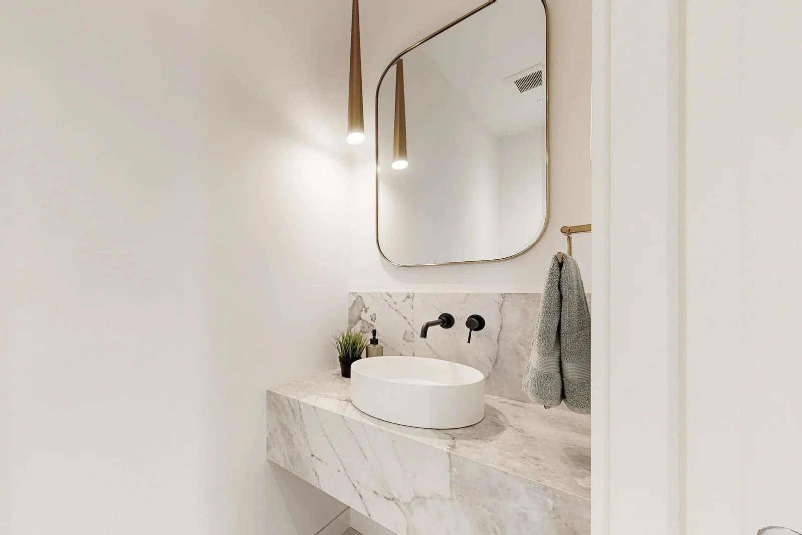 Powder room detail with floating marble vanity, vessel sink, matte black faucet, and twin brass pendants.
