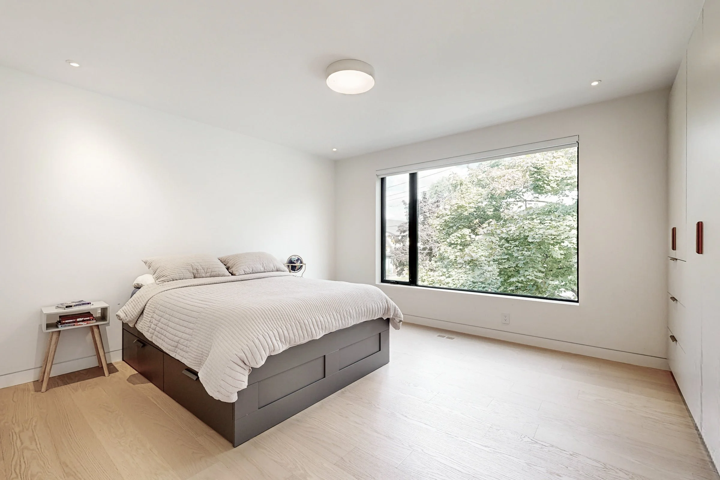 Bedroom with dark grey storage bed, built-in wardrobe, and a large black-framed picture window overlooking trees.