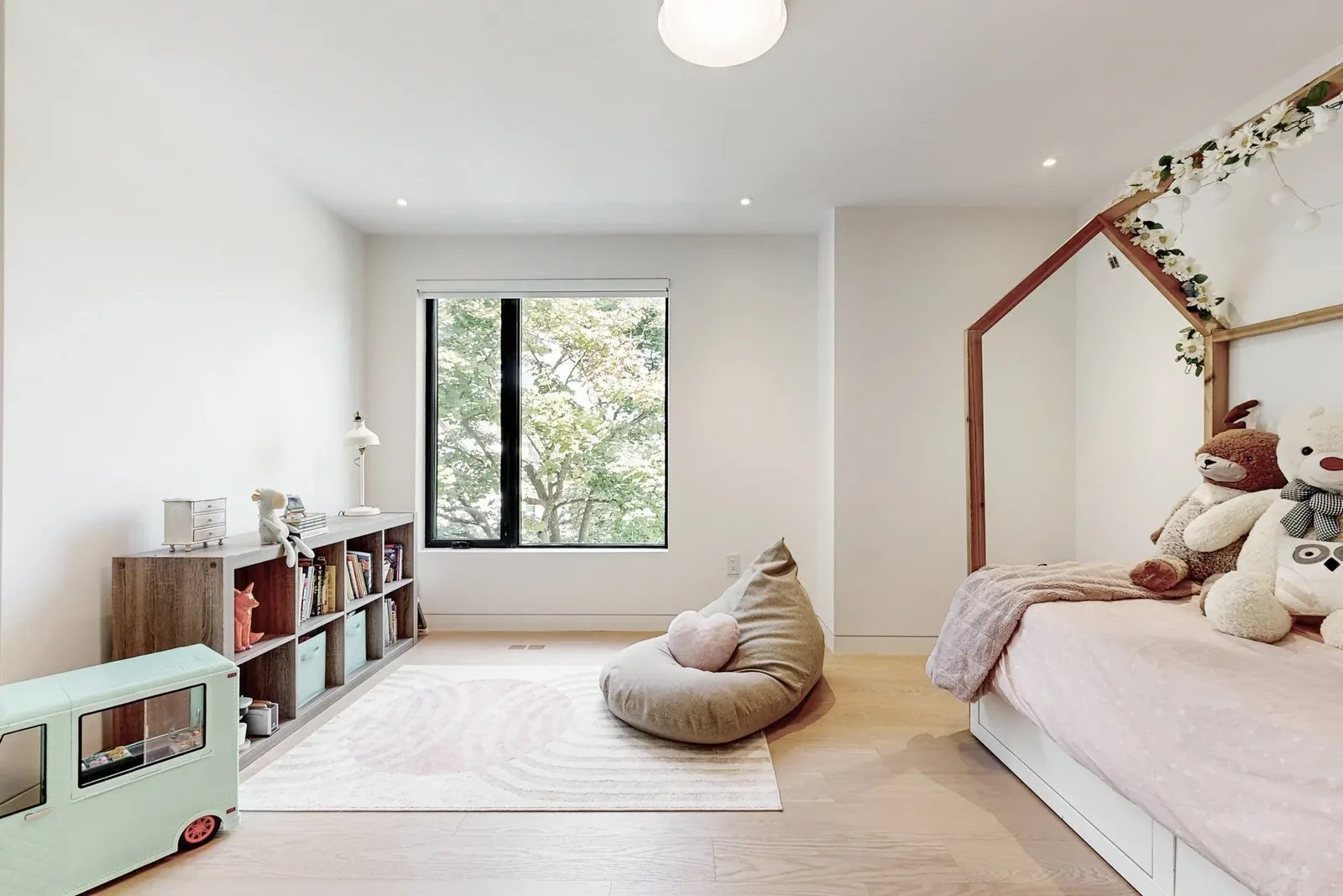 Child bedroom with white house-frame bed, pink bedding, bookcase cubbies, and beanbag reading nook by the window.