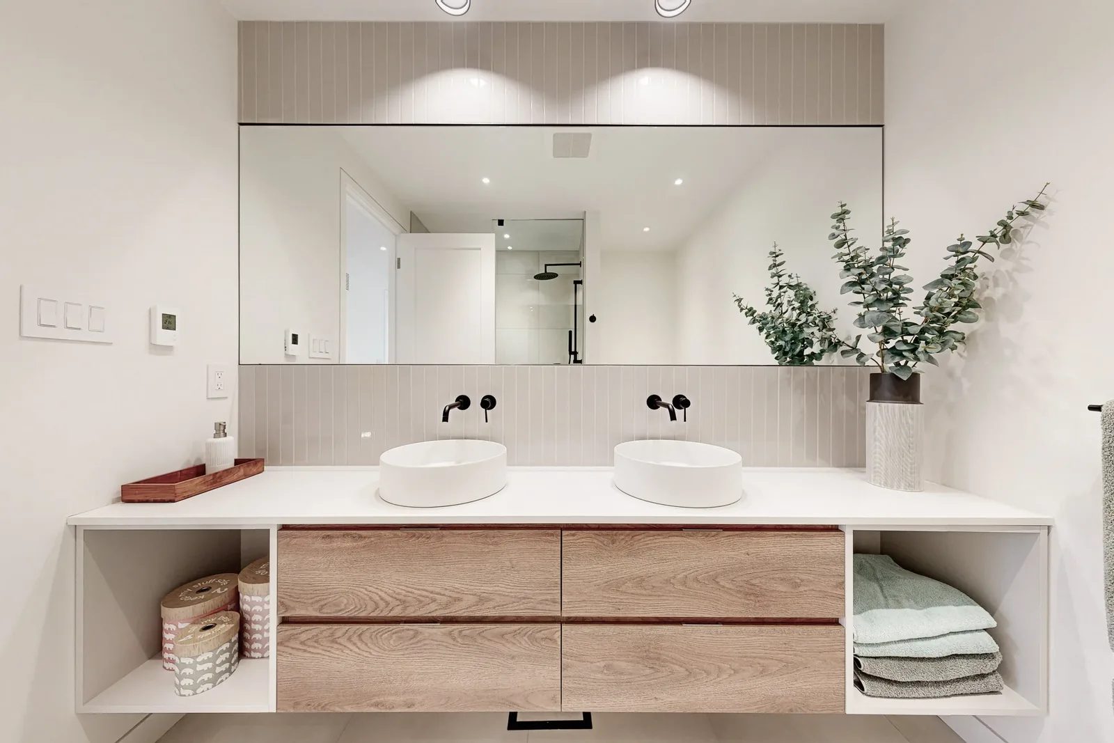 Floating oak double vanity with twin vessel sinks, matte black faucets, and a full-width mirror over fluted tile.