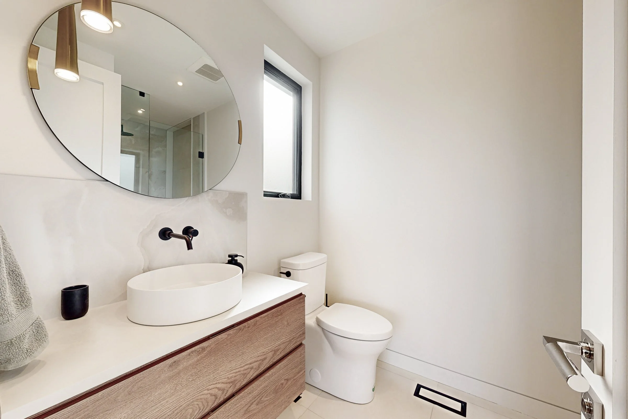 Powder room with floating oak vanity, onyx look stone slab and a round mirror flanked by brass pendants.