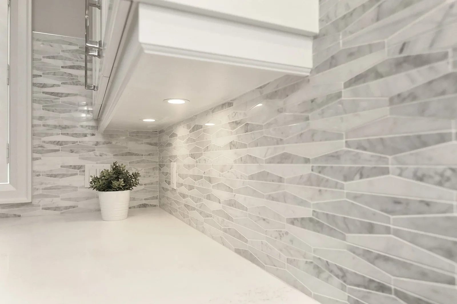 White kitchen counter with grey mosaic backsplash and under-cabinet lighting in a clean, finished detail shot.